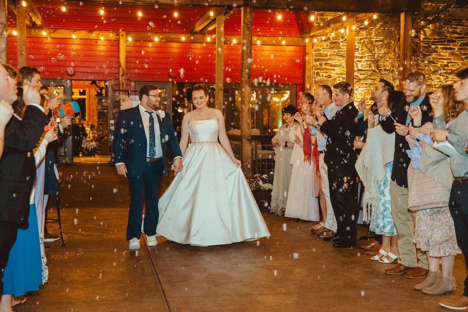Bride and groom exit through confetti tunnel surrounded by cheering guests at reception.