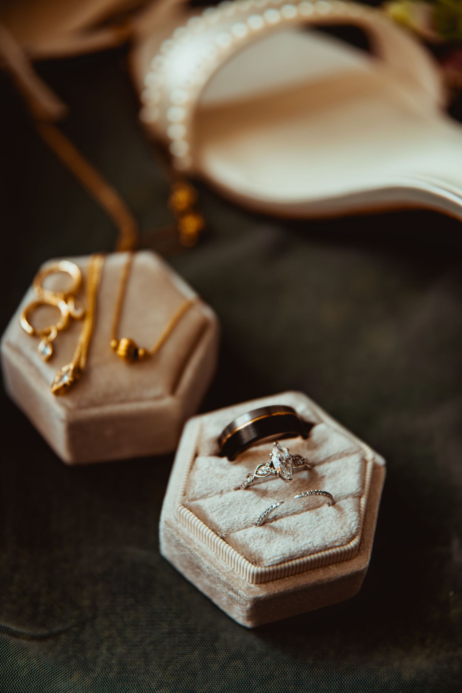Elegant wedding rings and gold jewelry displayed in velvet hexagonal boxes beside pearl bridal heels.