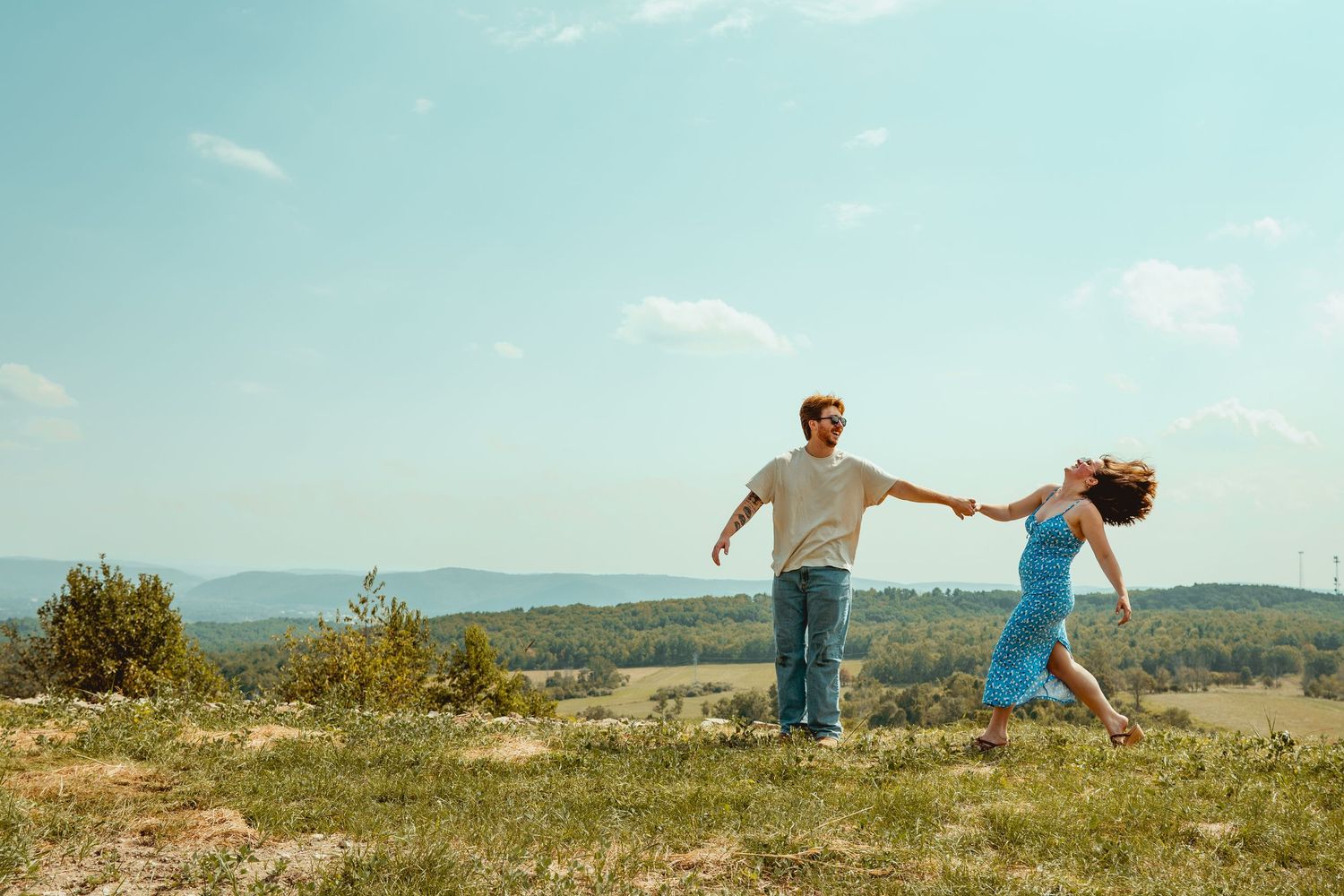 A person balances gracefully in a T-pose position on a grassy hilltop against a scenic mountain landscape.