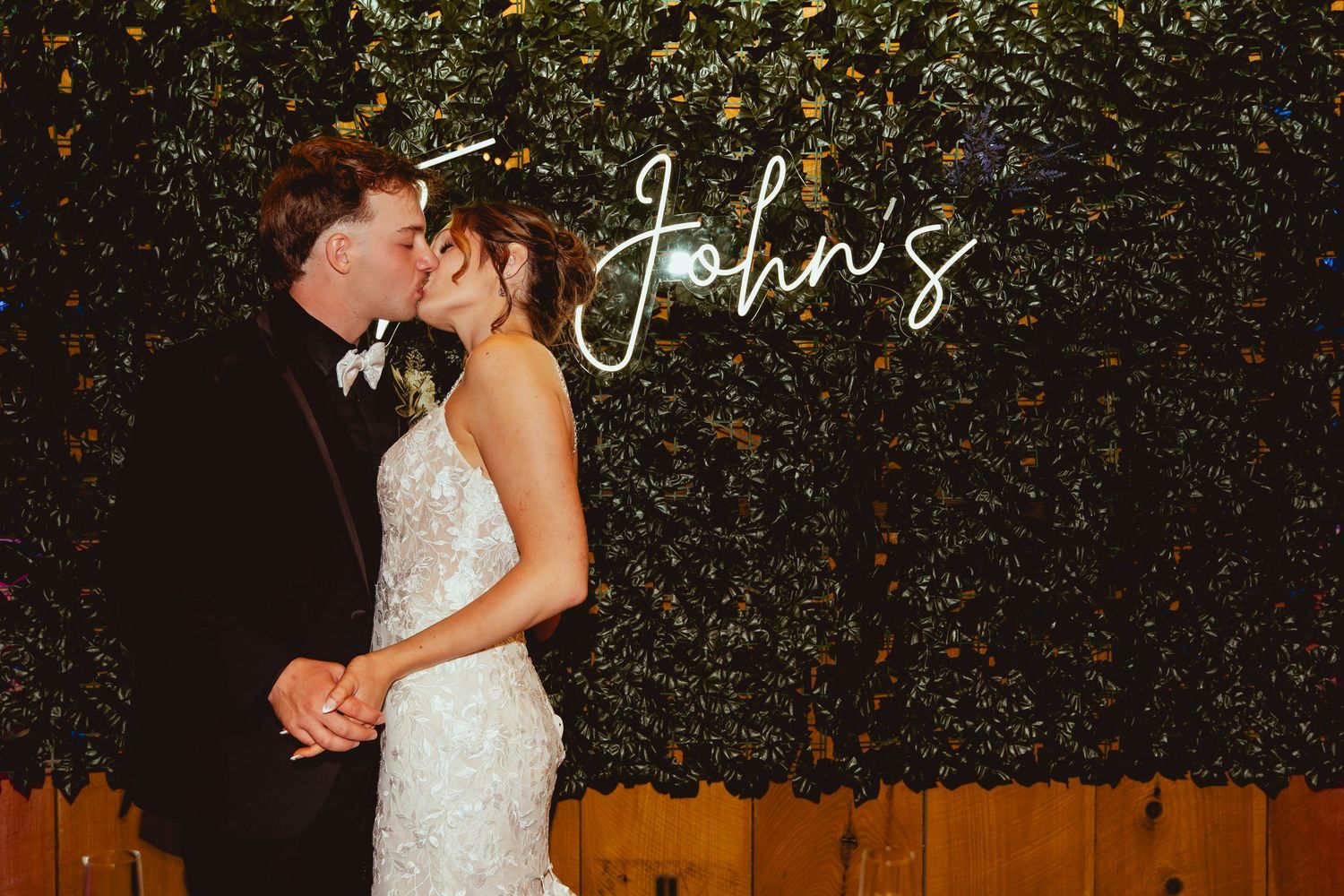 Elegant outdoor wedding ceremony setup with lush greenery wall backdrop and white floral arrangements.