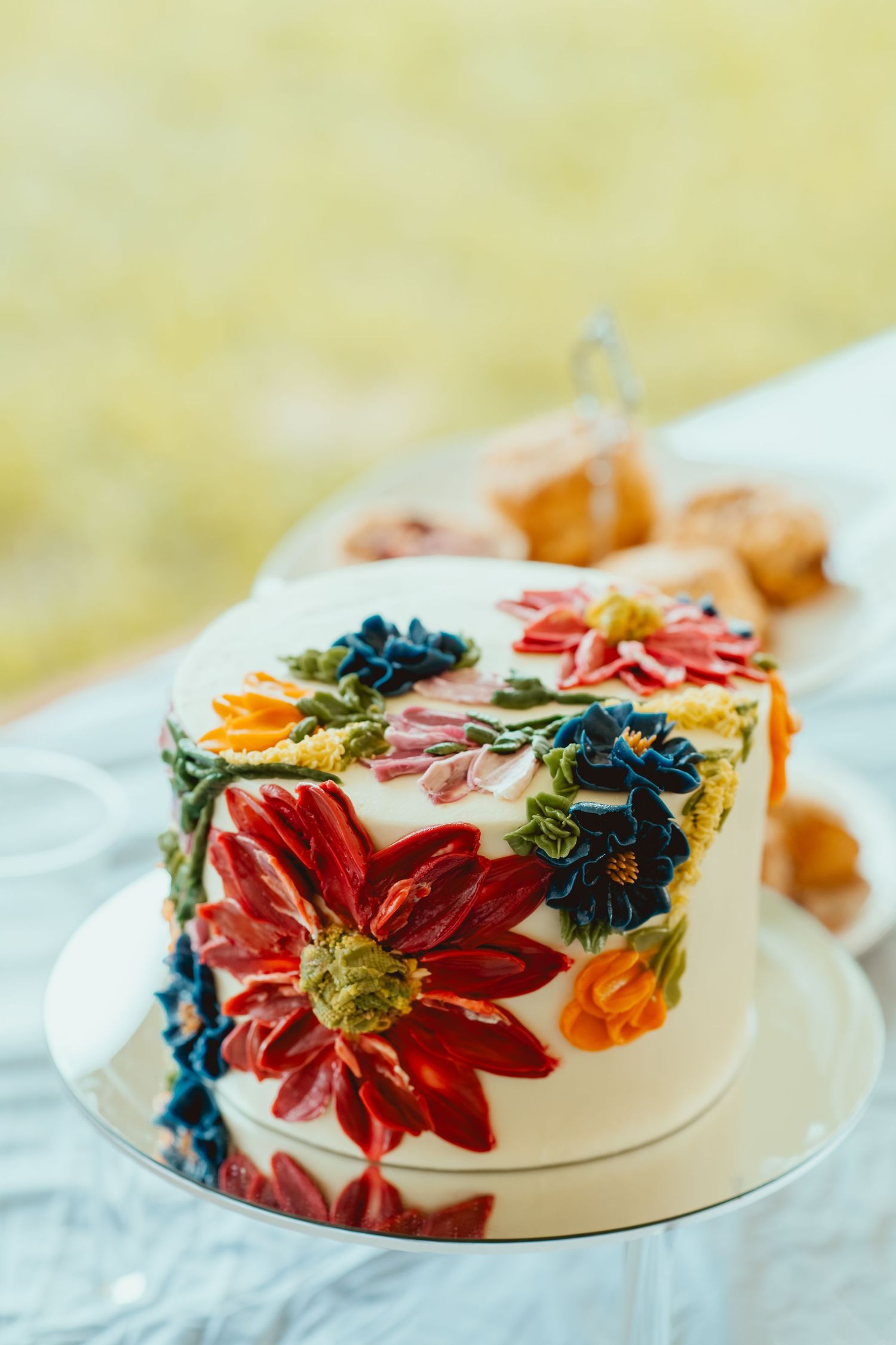 White wedding cake decorated with vibrant pressed flowers in red, orange and blue colors.