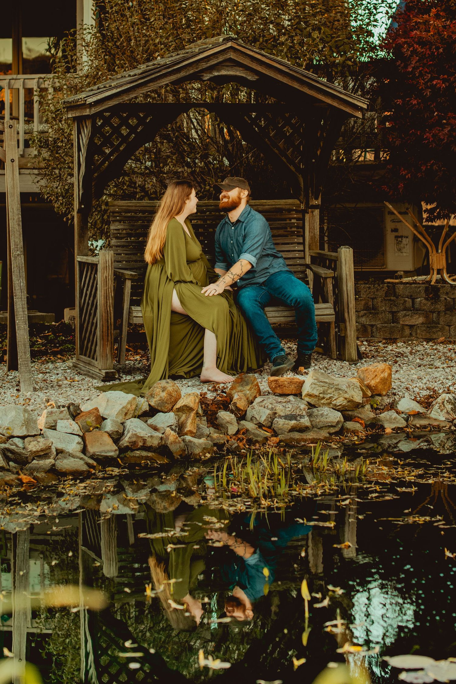 A couple sits by a reflective pond surrounded by autumn leaves creating a romantic mirrored scene in nature.