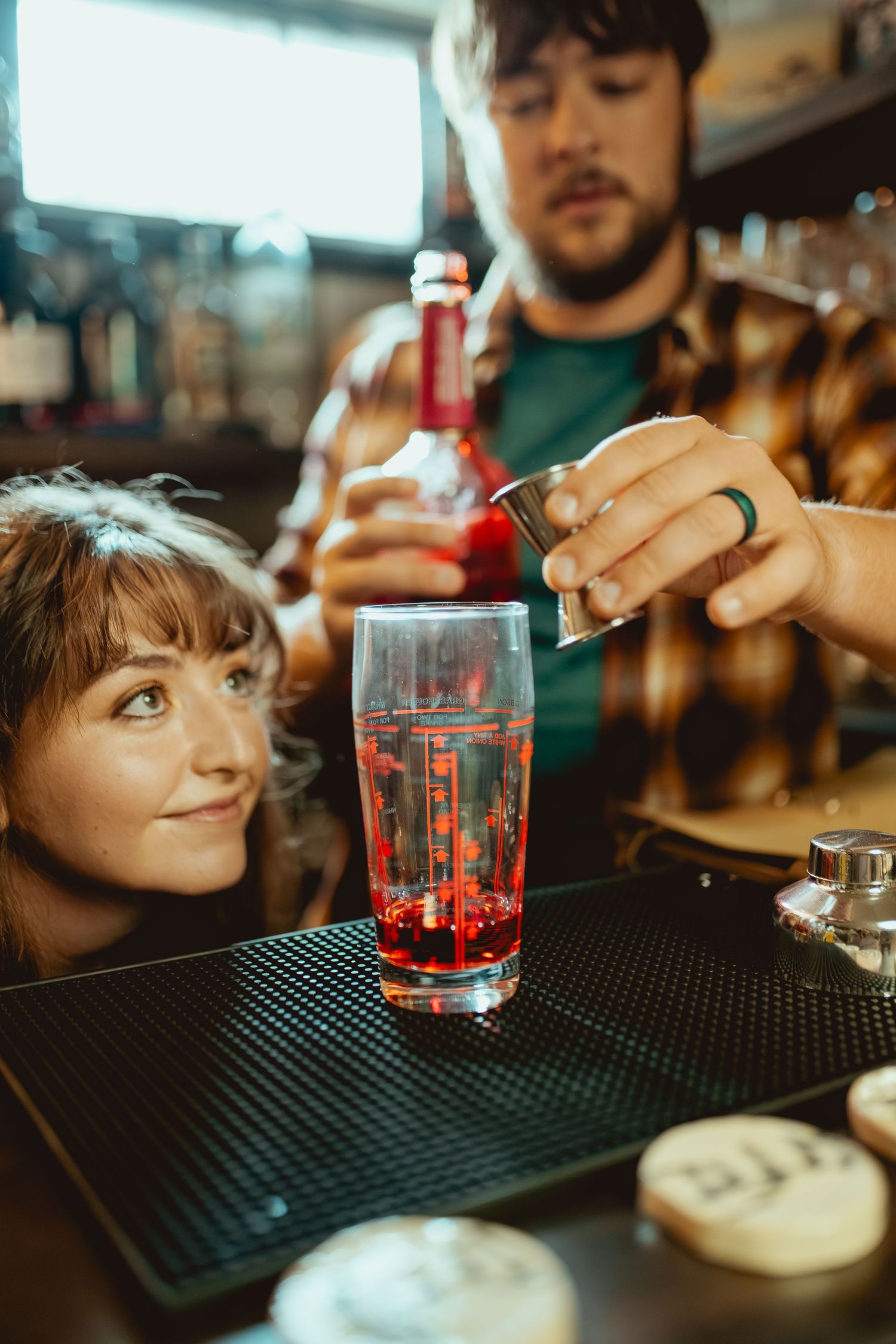 Bartender preparing cocktails on a black rubber bar mat with red liquid in a glass.