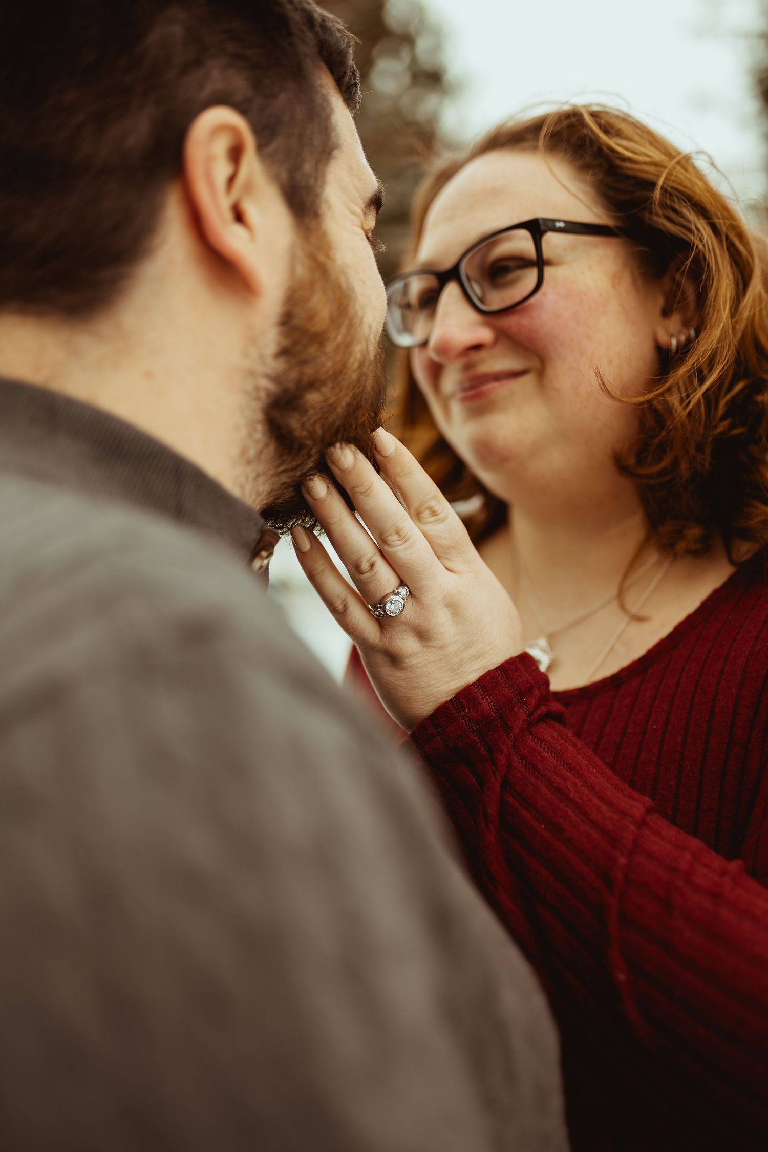A couple shares an intimate moment in a romantic engagement photoshoot wearing burgundy and gray.