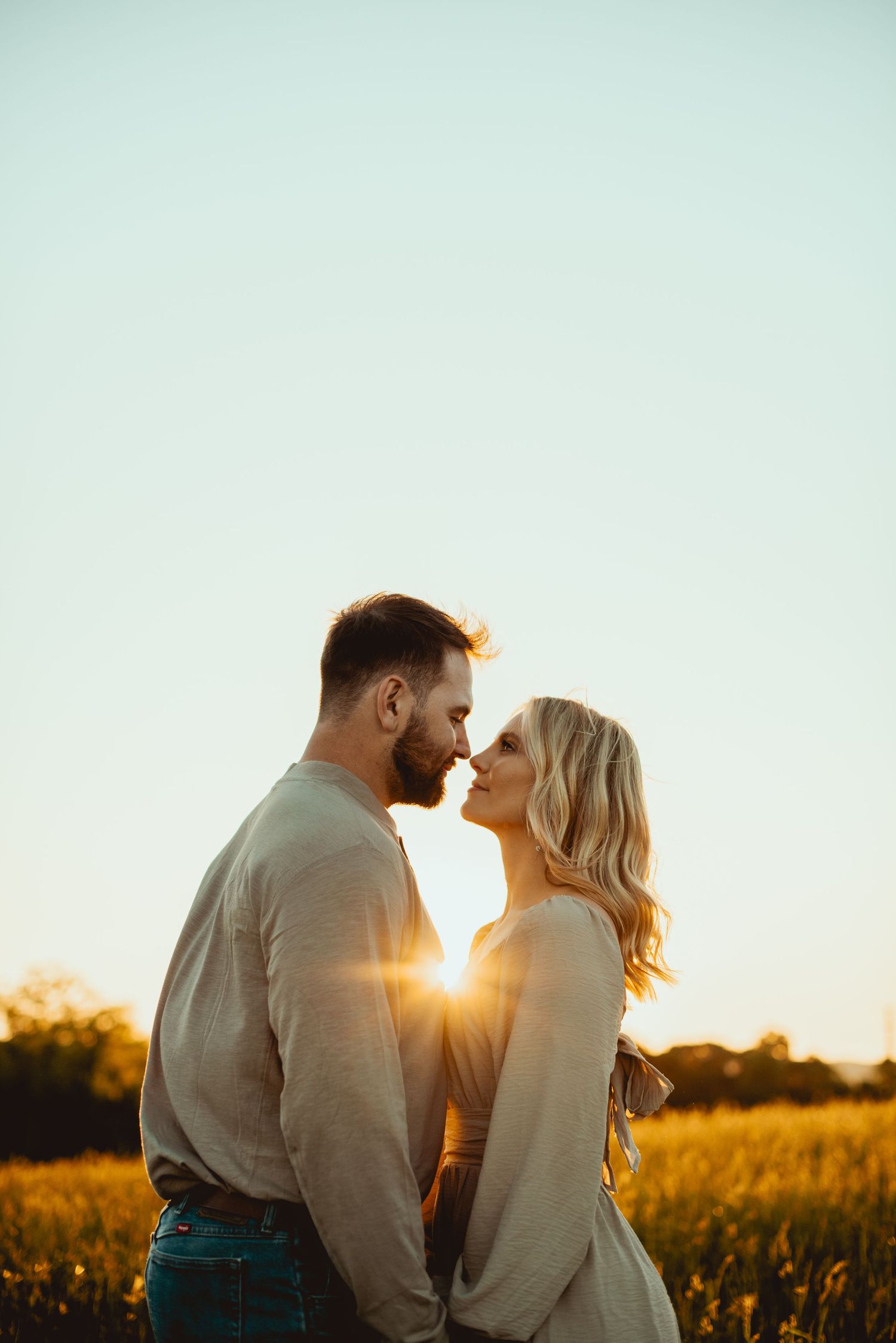 Romantic couple shares intimate moment in golden sunlit field during sunset.