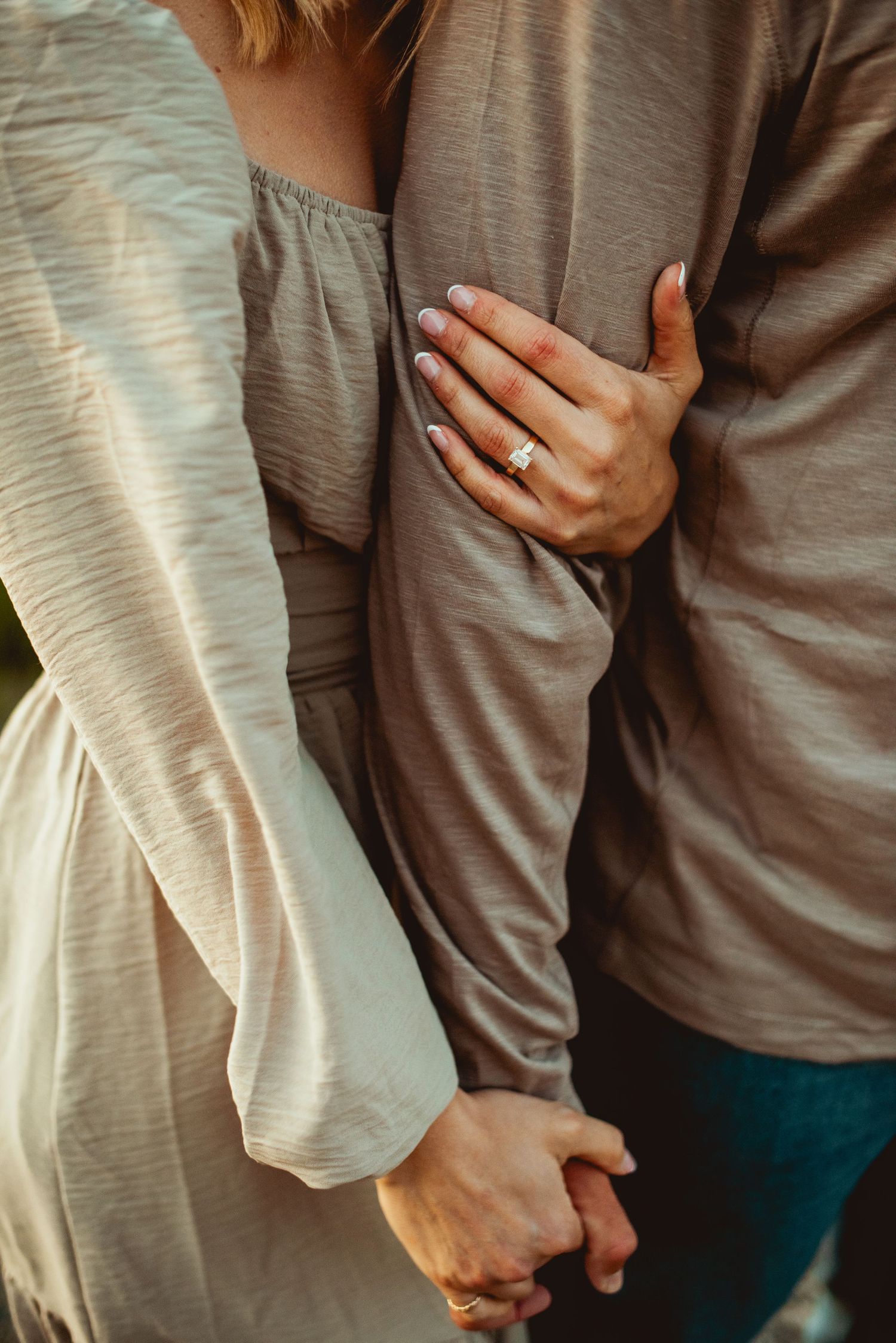 Close-up shot of hands holding with engagement ring visible in soft natural light.