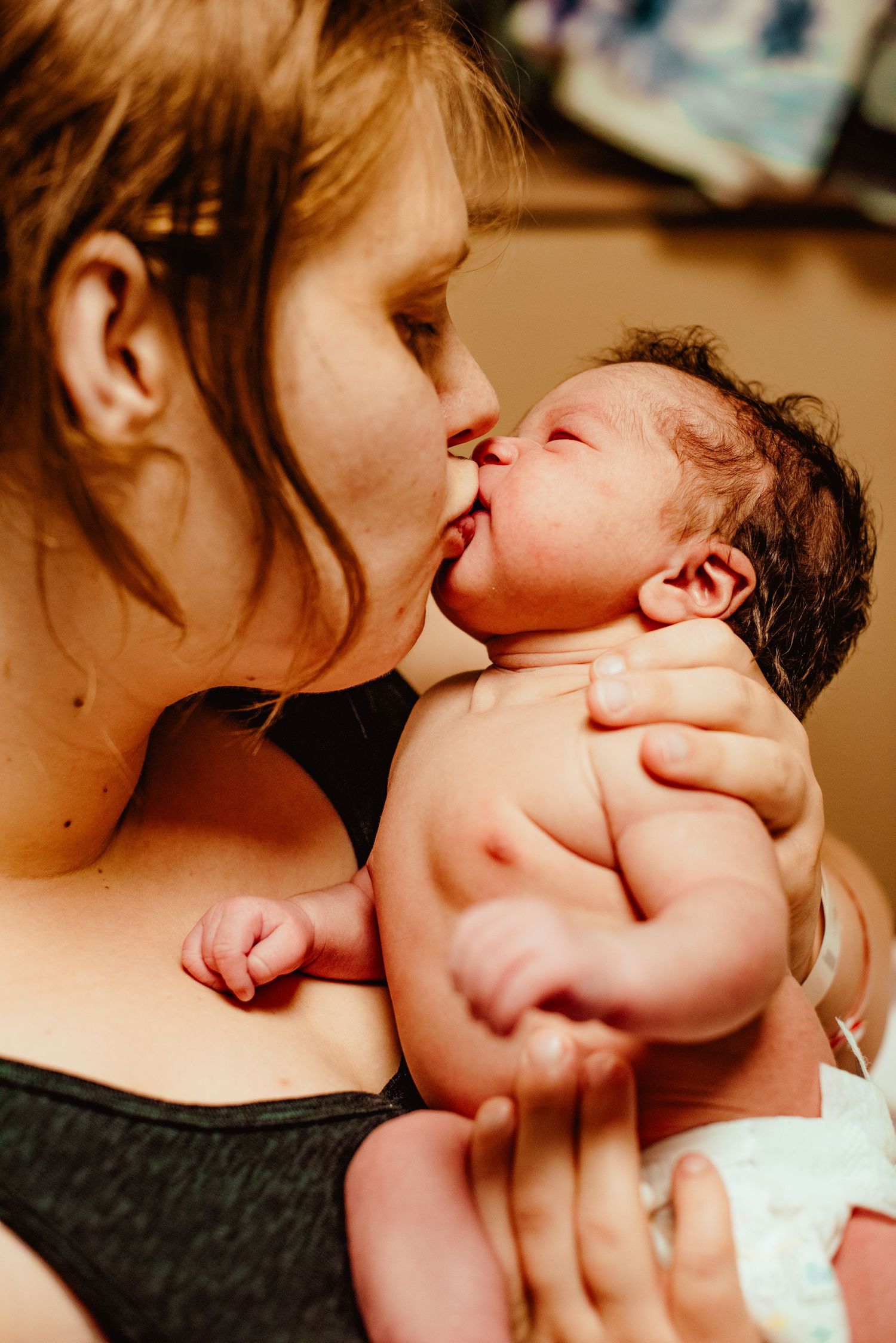 A tender moment shows a parent gently kissing a baby's cheek in warm lighting.