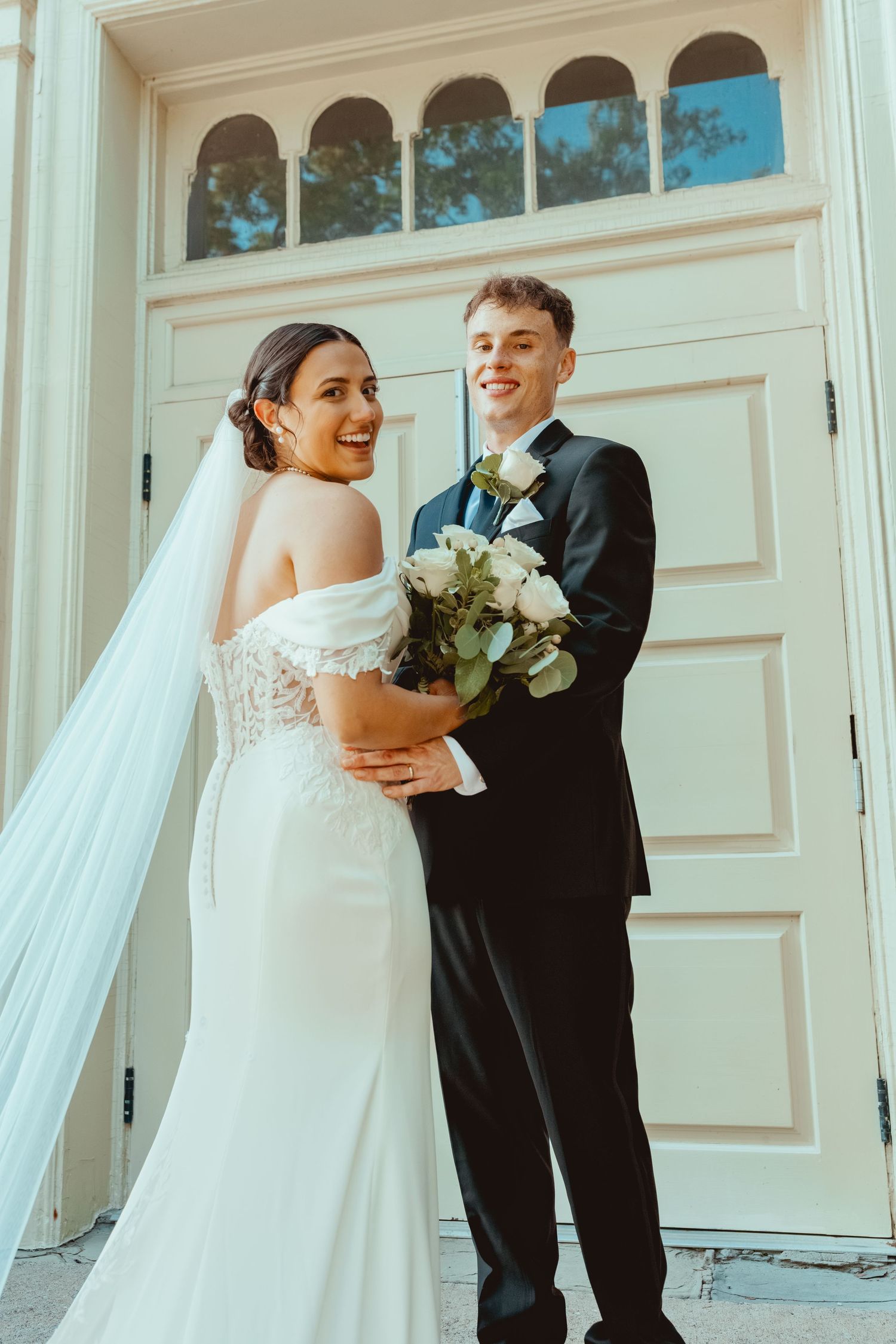 Couple sharing joyful moments outside elegant white building during wedding photoshoot.