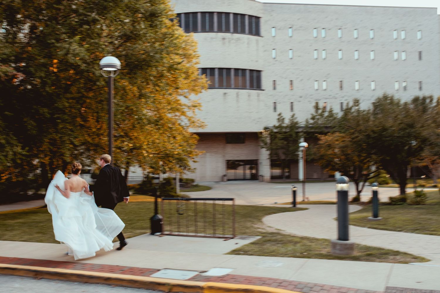 Wedding couple poses near a modern building on a fall day with golden leaves on trees.