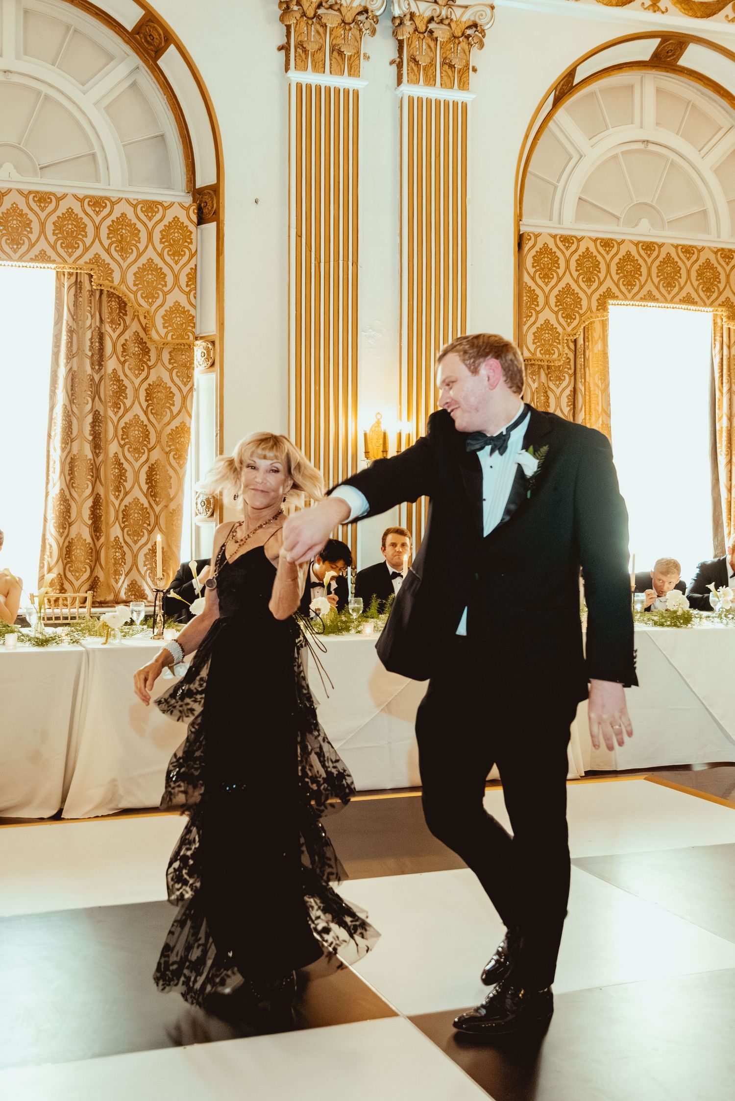 Couples dancing together in an elegant ballroom with ornate gold decor and patterned walls.