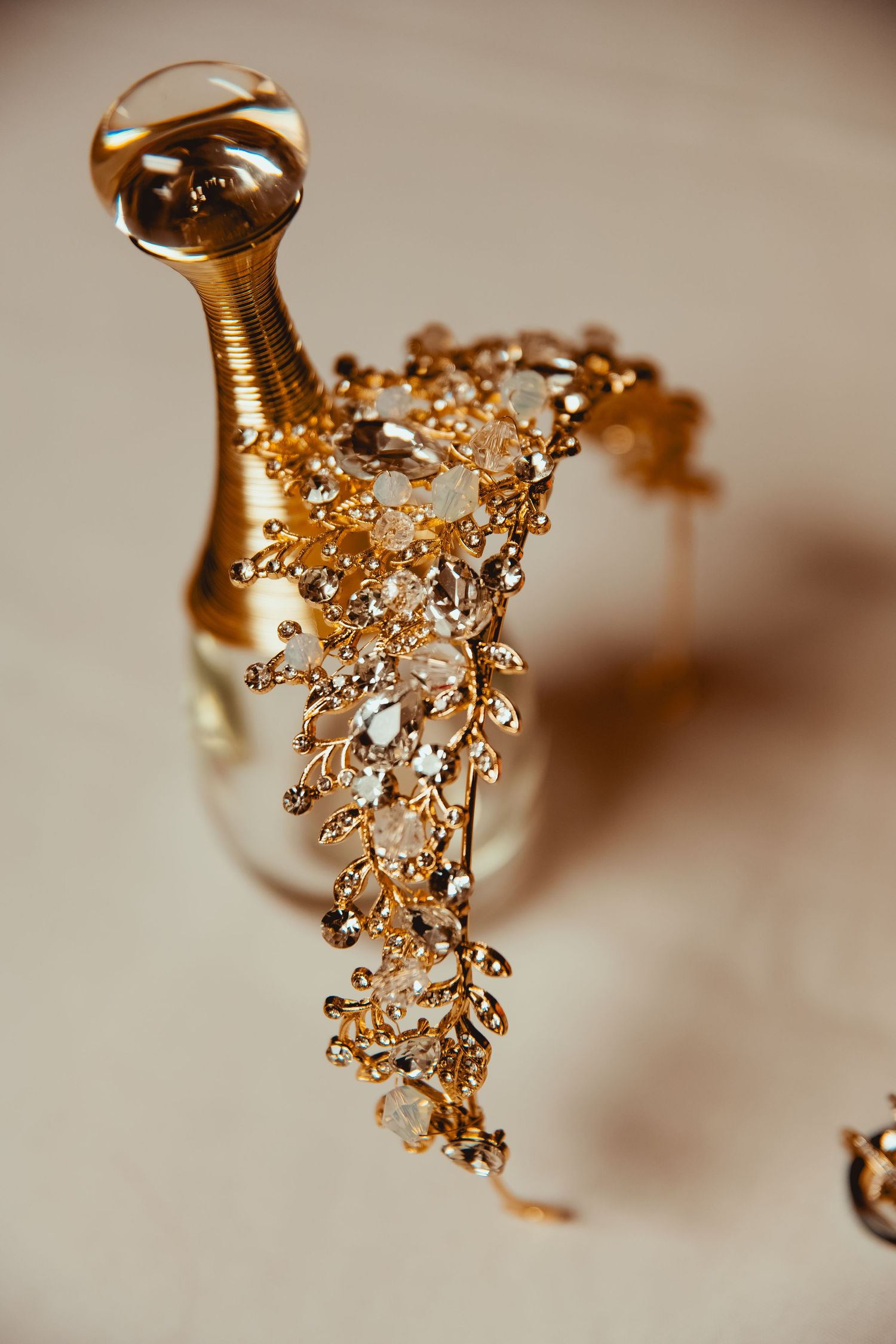 Elegant gold crystal bridal headpiece resting against a gold Dior perfume bottle on a neutral background.