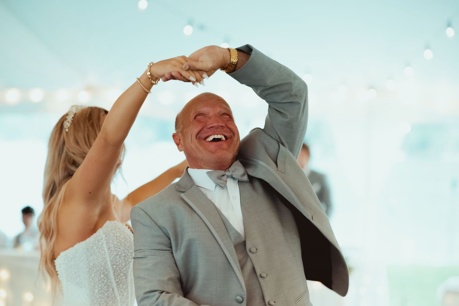Bald father of bride laughing joyfully while dancing with bride at wedding reception.