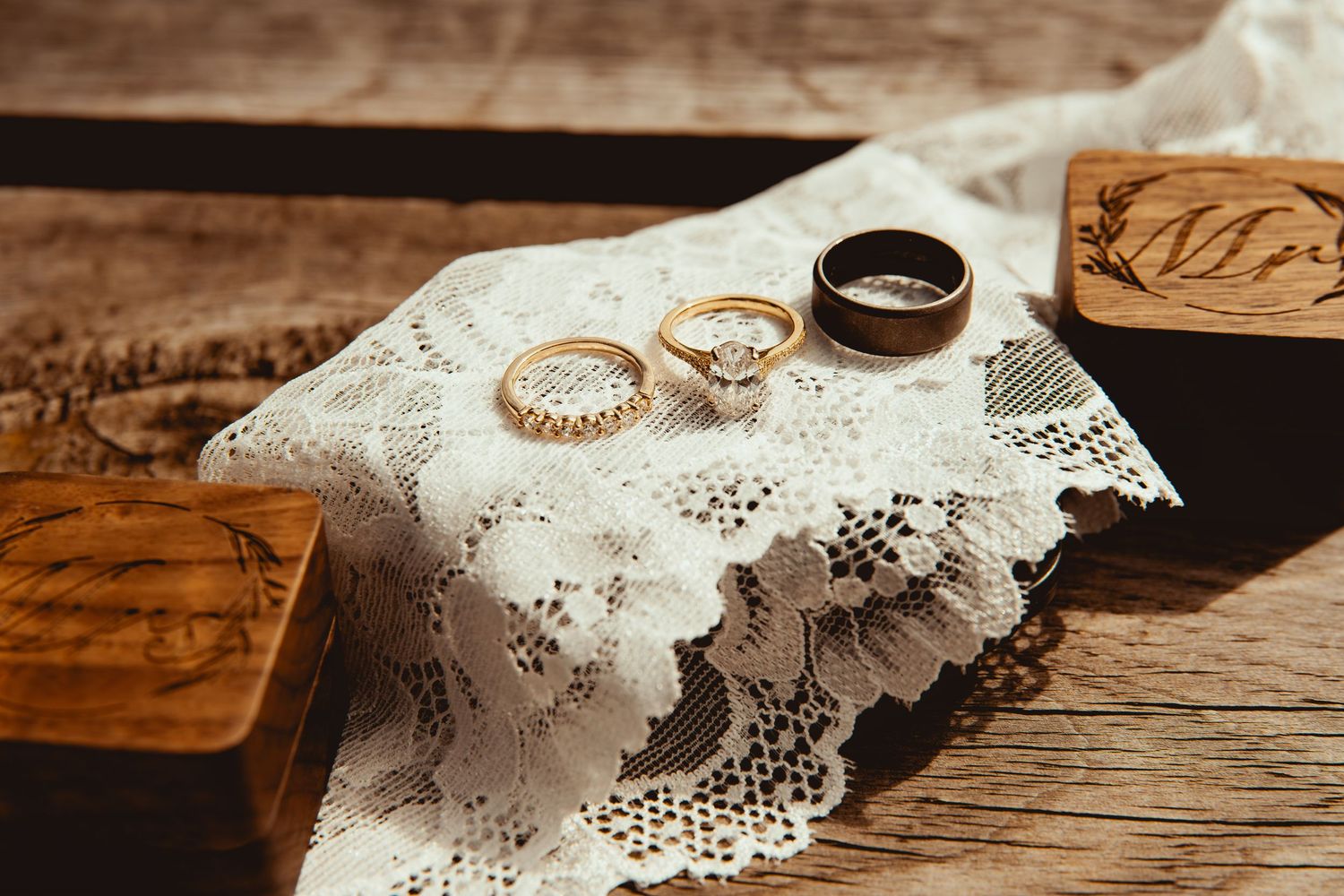 Wedding rings and delicate lace details rest on a rustic wooden surface.
