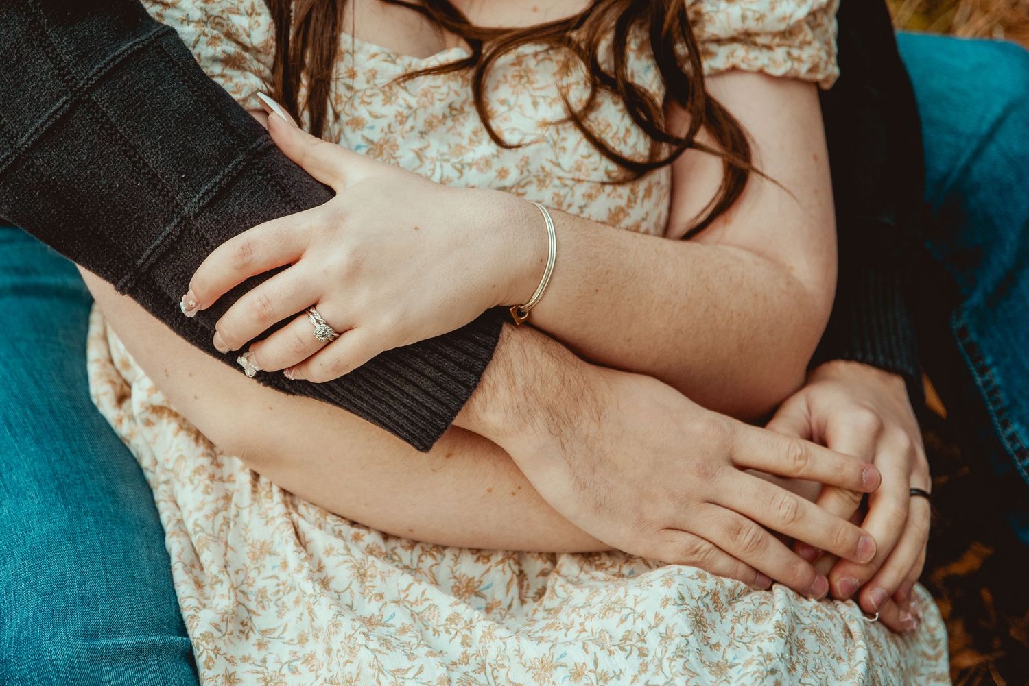 Cropped close-up view of hands gently resting on knees while sitting on a teal colored couch.