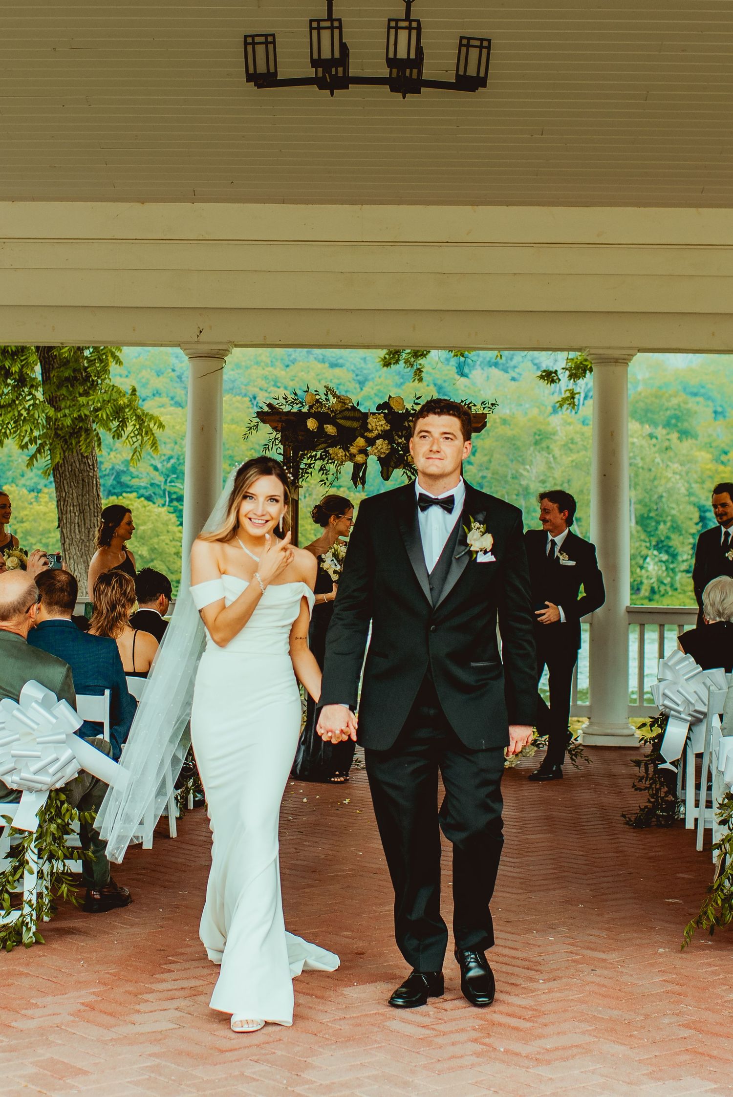 Newlyweds walking down aisle together under covered porch decorated with lanterns.