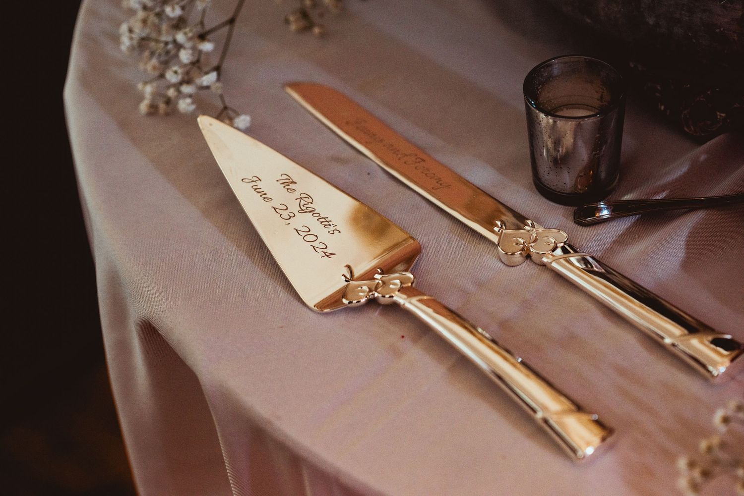 Gold-handled wedding cake knife and server set rests elegantly on a cream tablecloth with scattered crystal decorations.