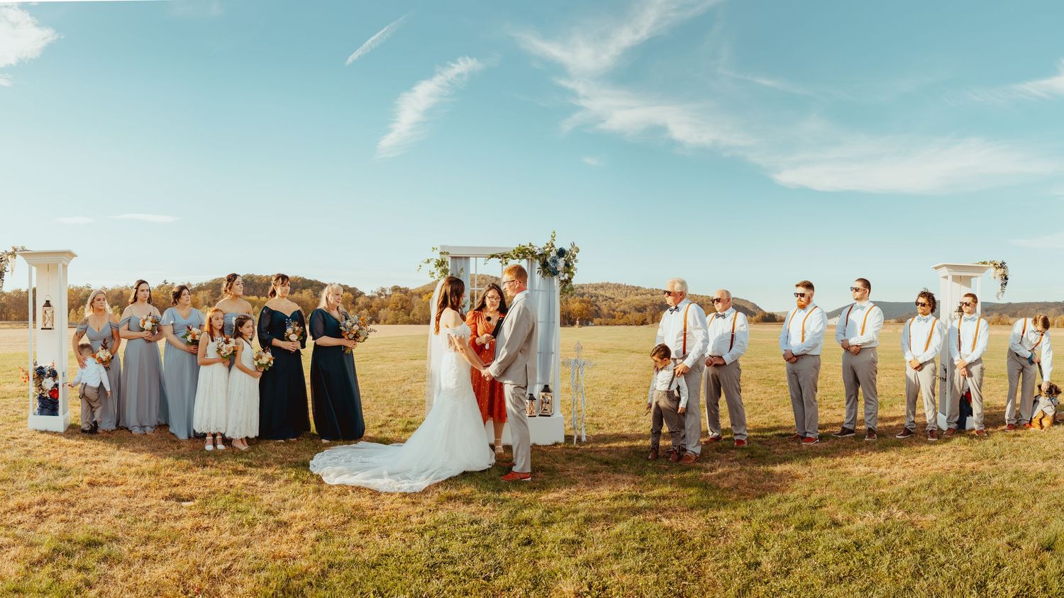 Panoramic view of an outdoor wedding ceremony setup in a vast field under blue skies.