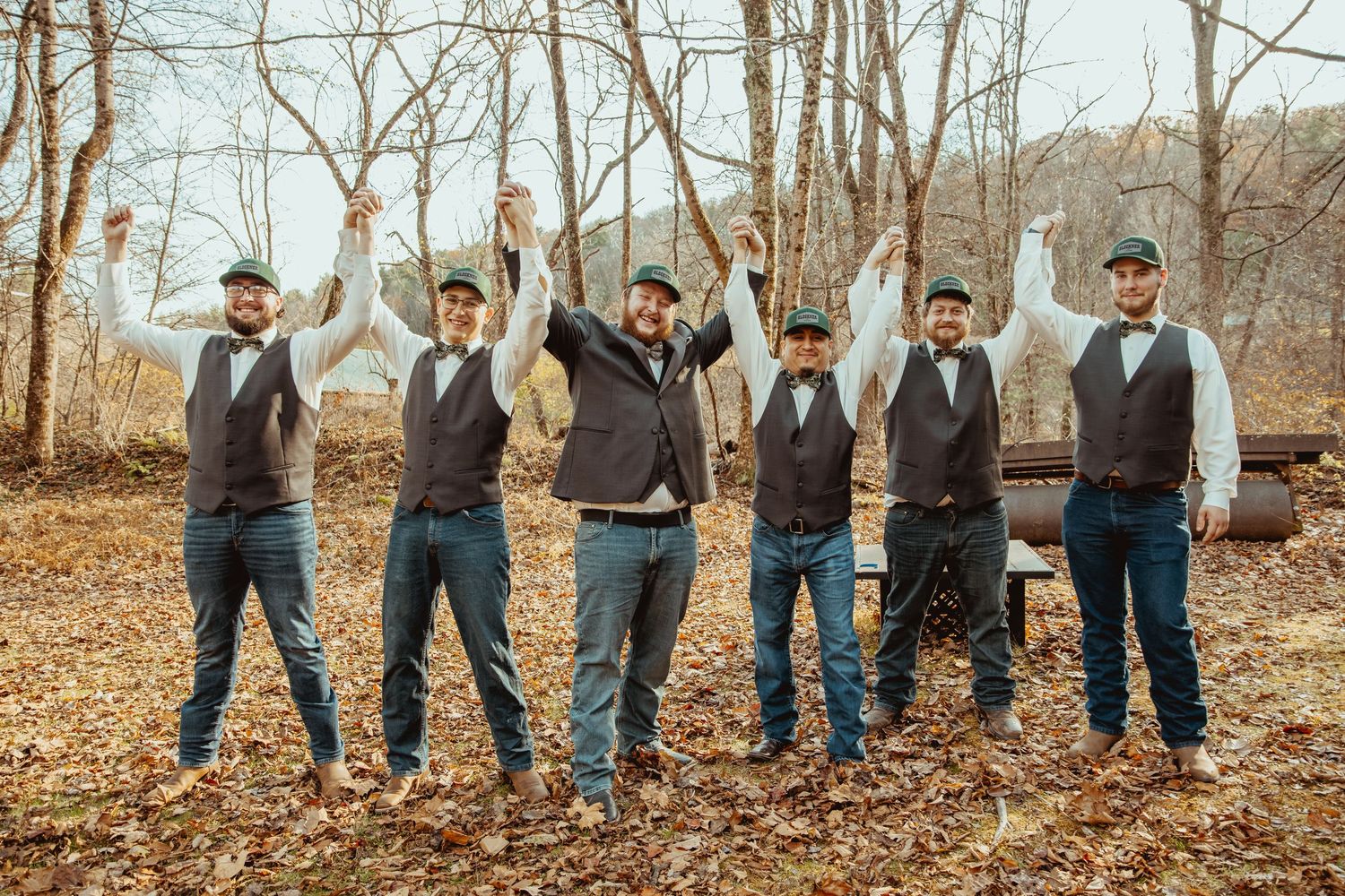 A group in matching gray suits and blue ties pose together in a wooded autumn setting.