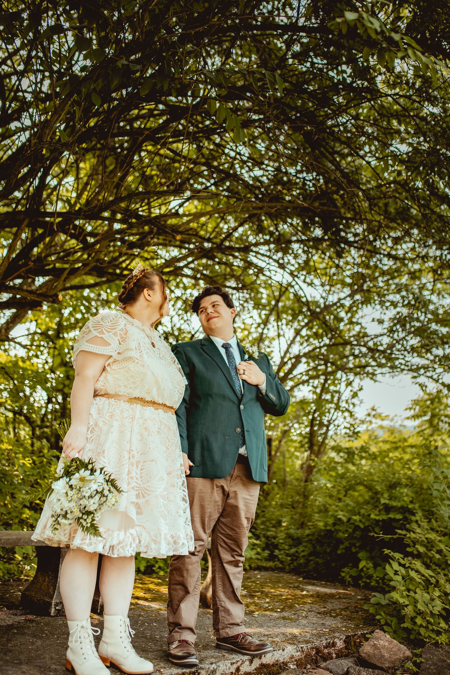 A couple's feet stand together on a stone path under green trees during an outdoor wedding photoshoot.