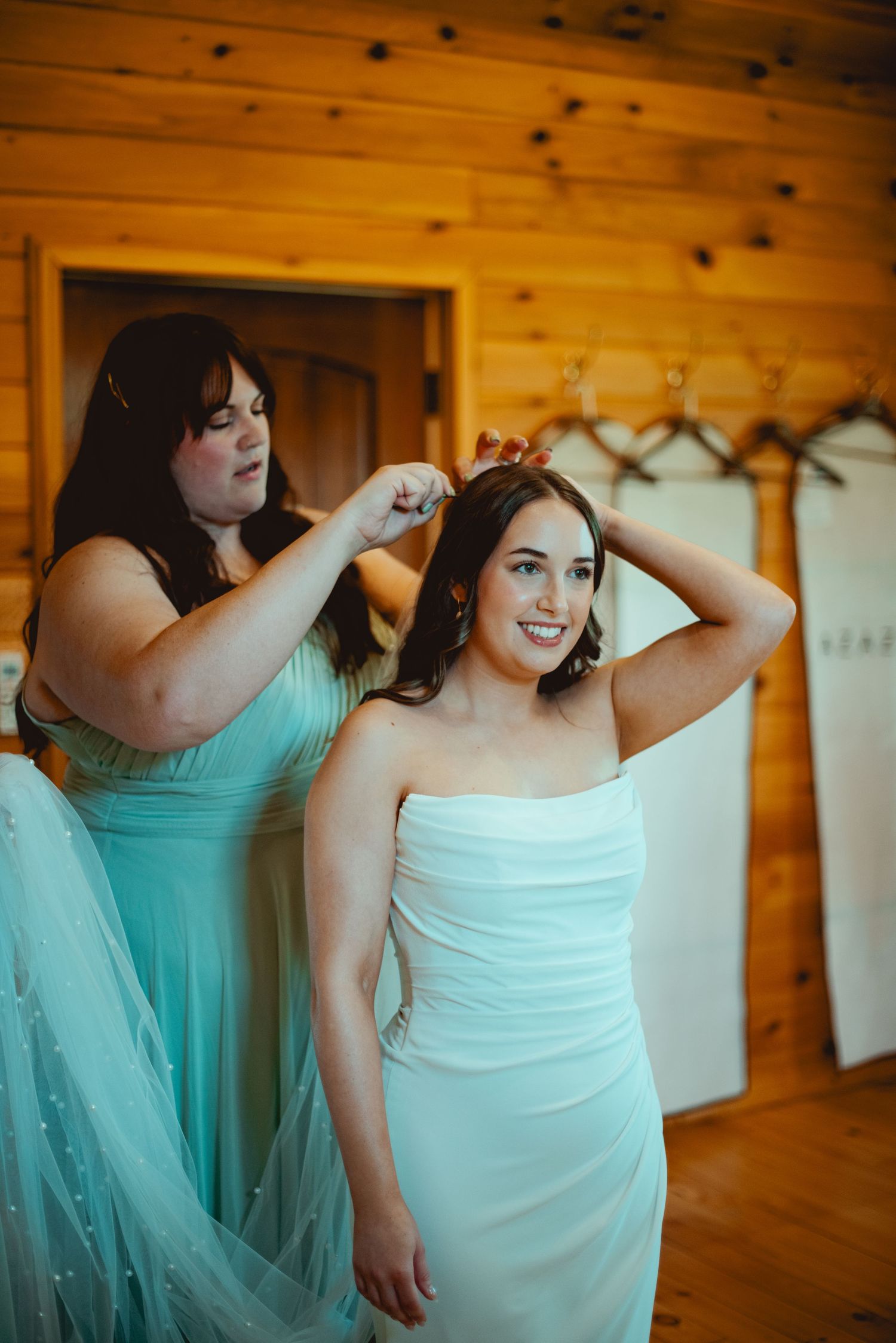 Preparations in a wooden cabin as bridesmaids in mint dresses help with wedding day styling.