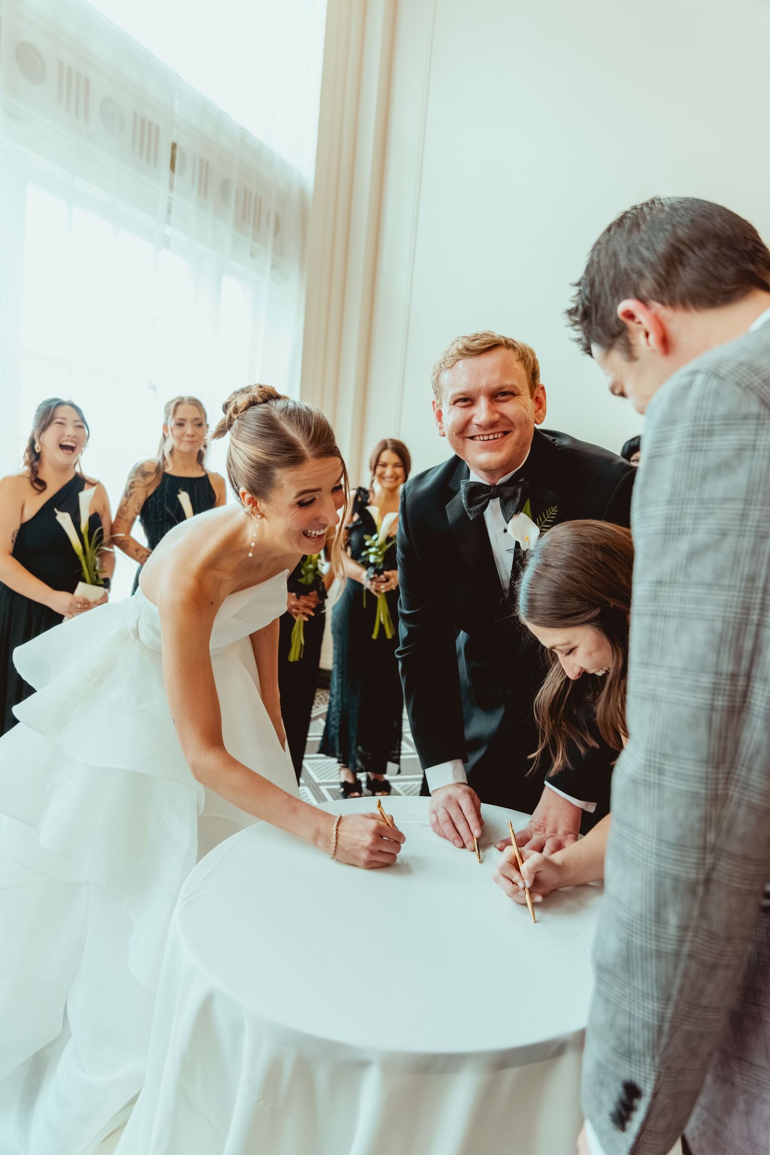 Wedding guests gathered around to sign the marriage certificate at an elegant indoor ceremony.