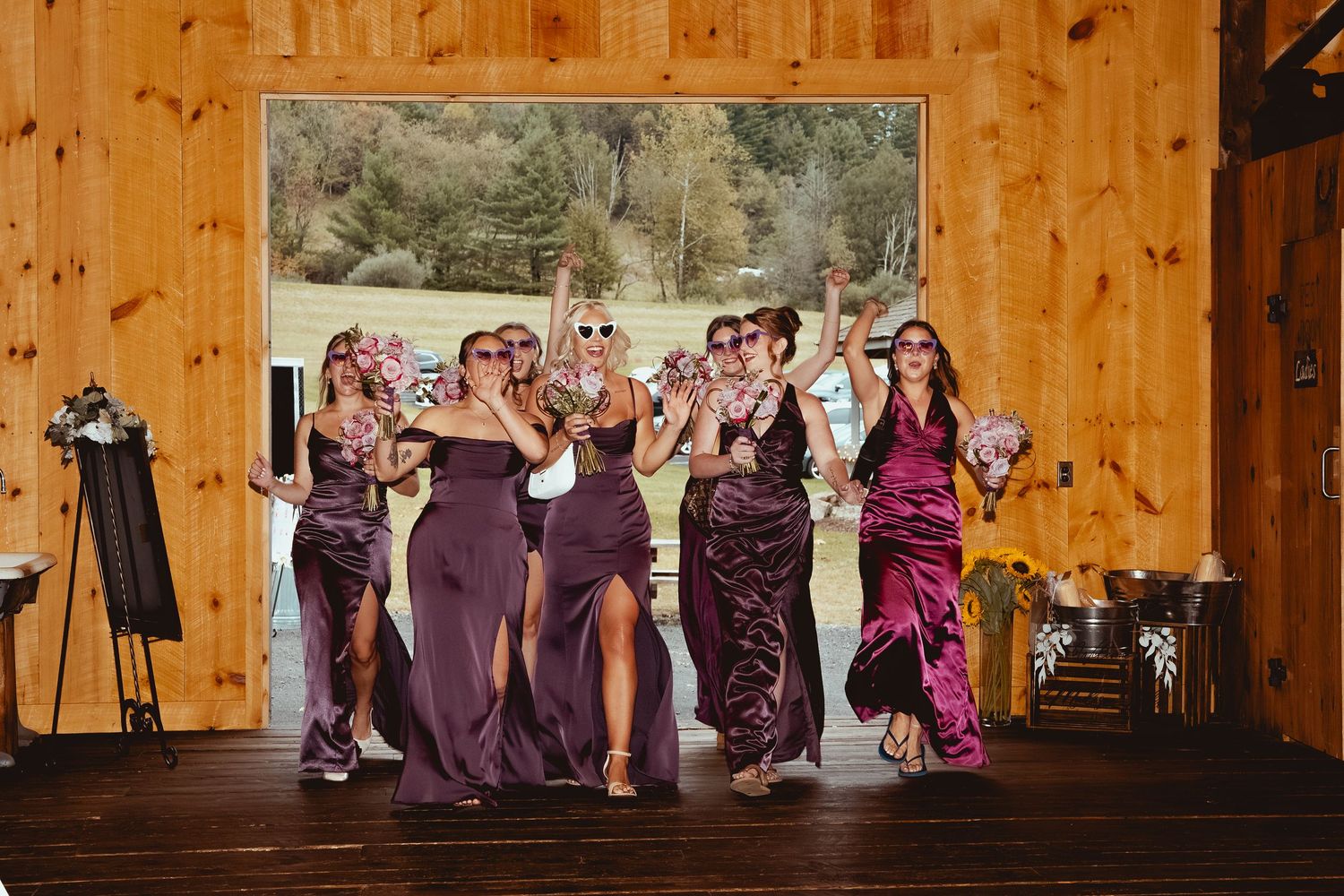 Wedding party poses in a rustic wooden barn venue with purple bridesmaid dresses and warm interior lighting.