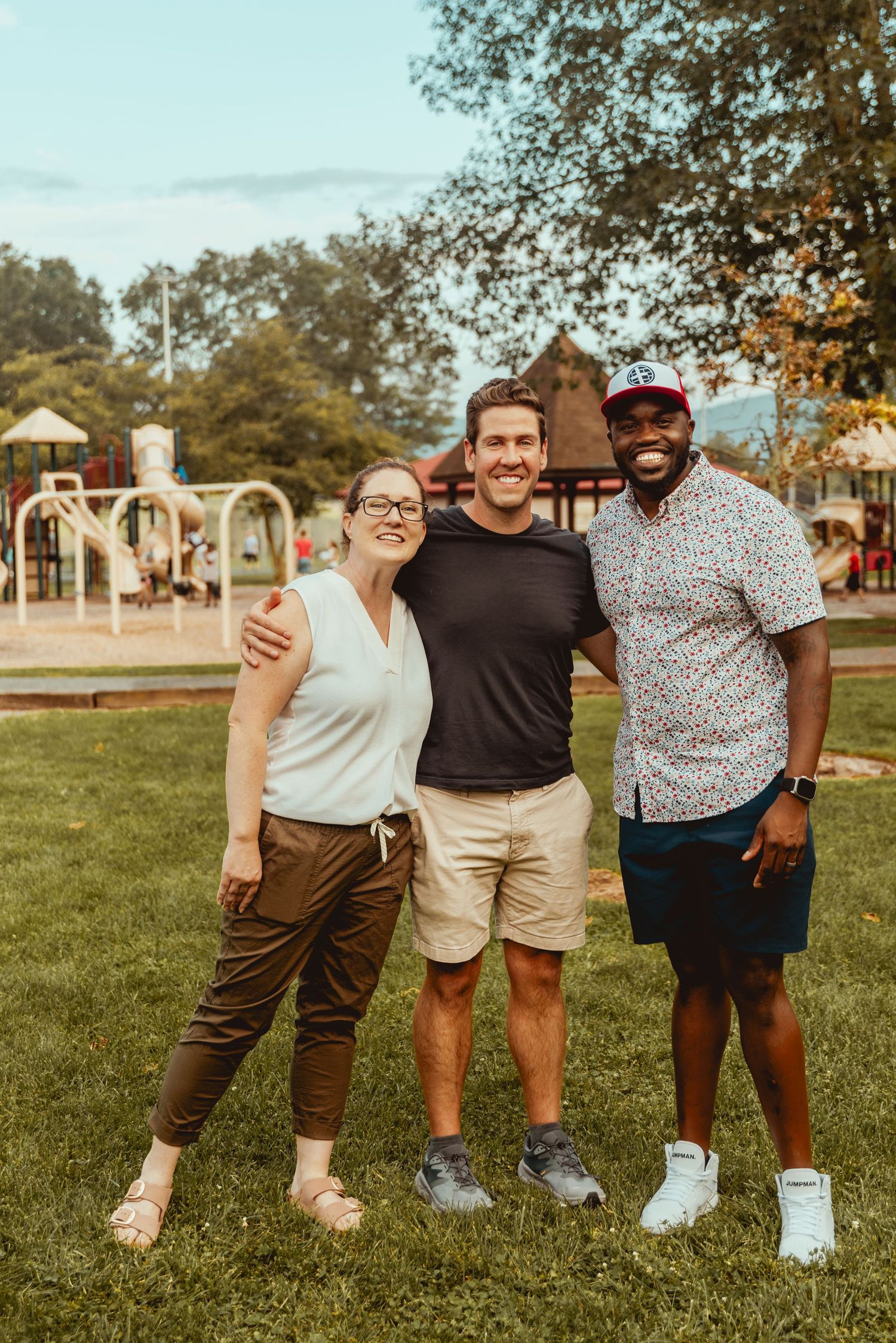 A group of friends smile together while posing outdoors on a grassy lawn during golden hour.