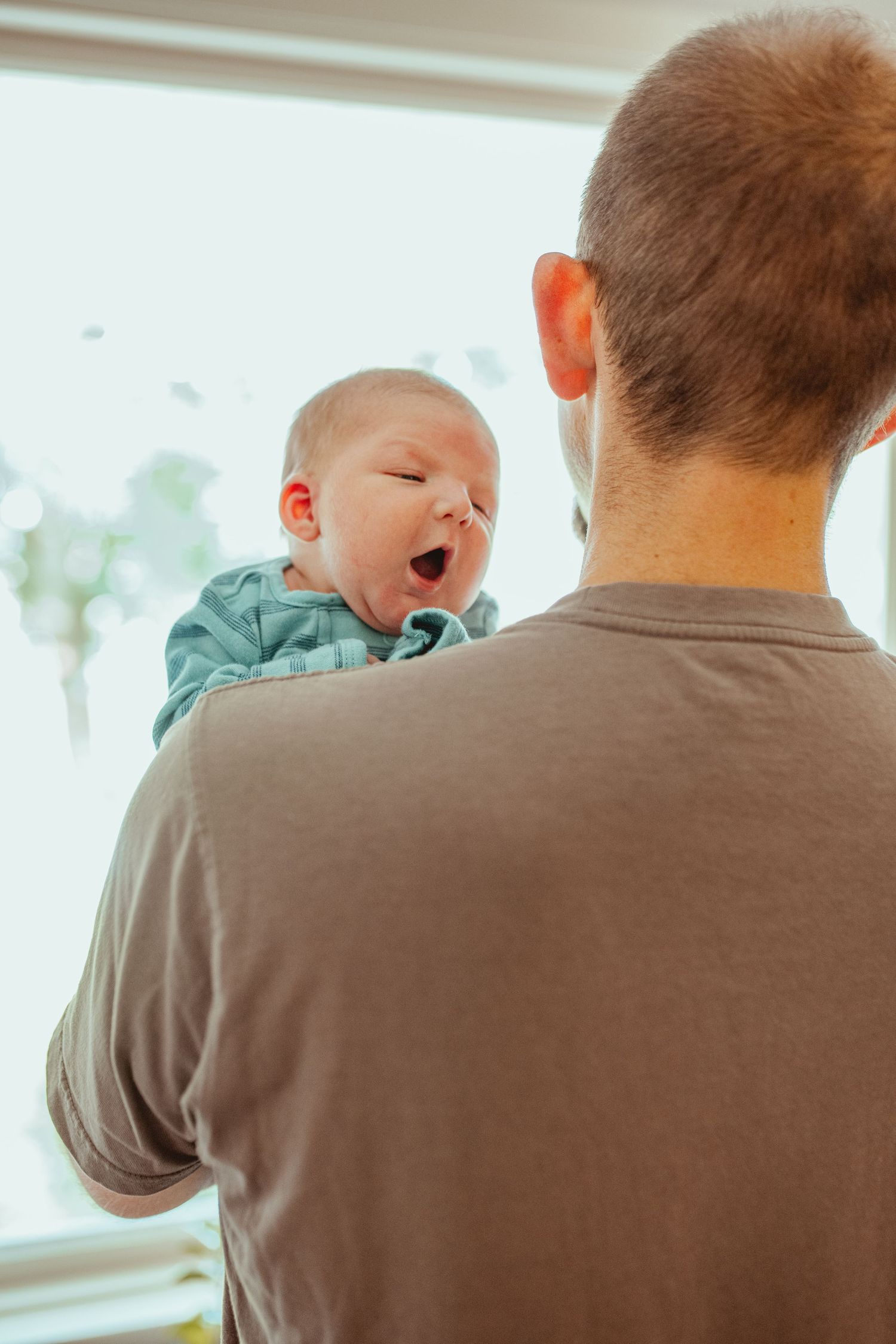 A series of four progressive photos showing a baby yawning while being held against someone's shoulder.