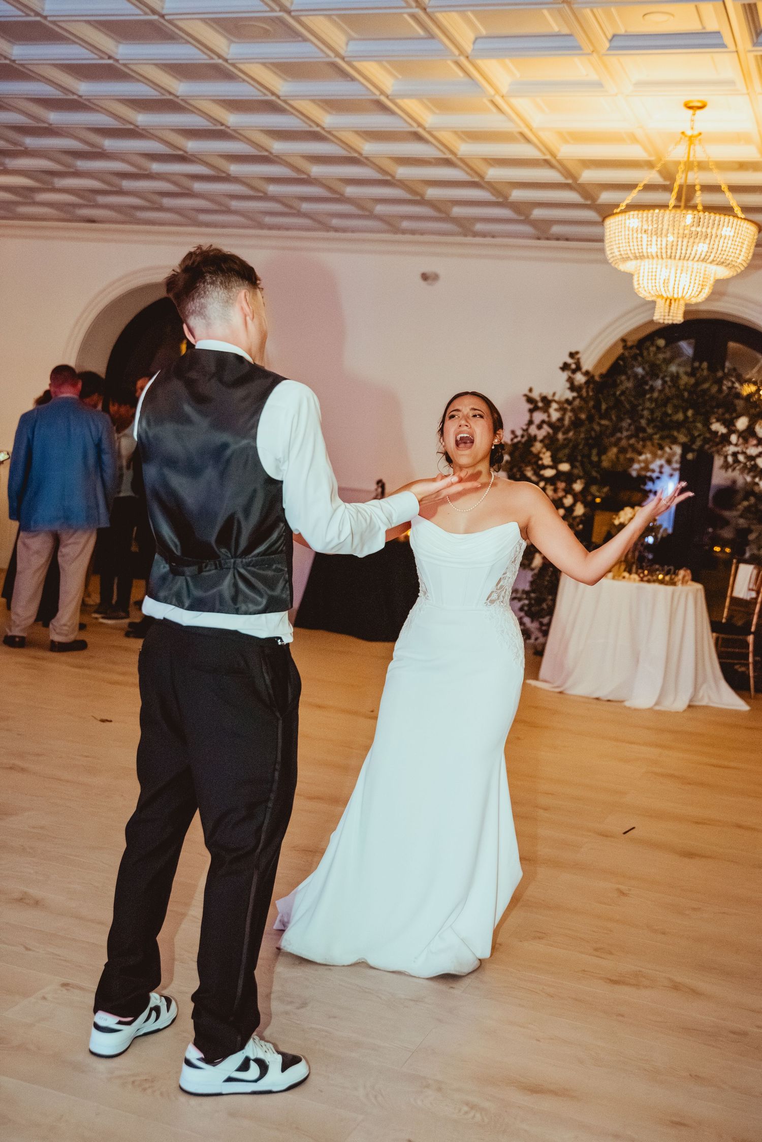Wedding reception dance floor with couples dancing under ornate ceiling and chandelier.