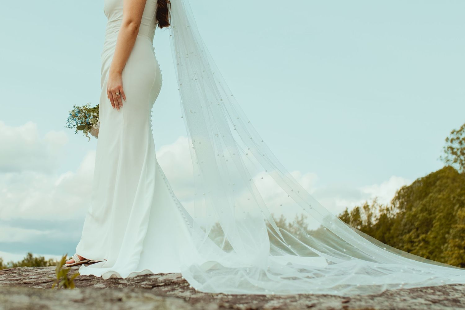 Flowing white wedding veil trailing across rocky surface with mountains in background.