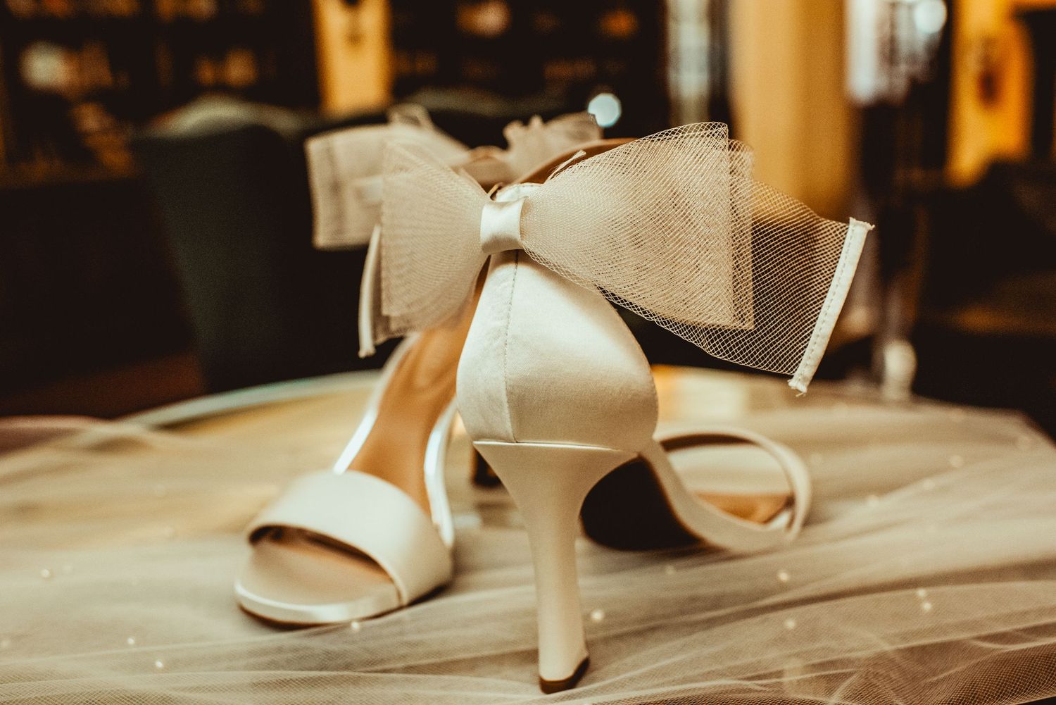 Cream colored bridal heels displayed on a wooden surface with warm lighting.