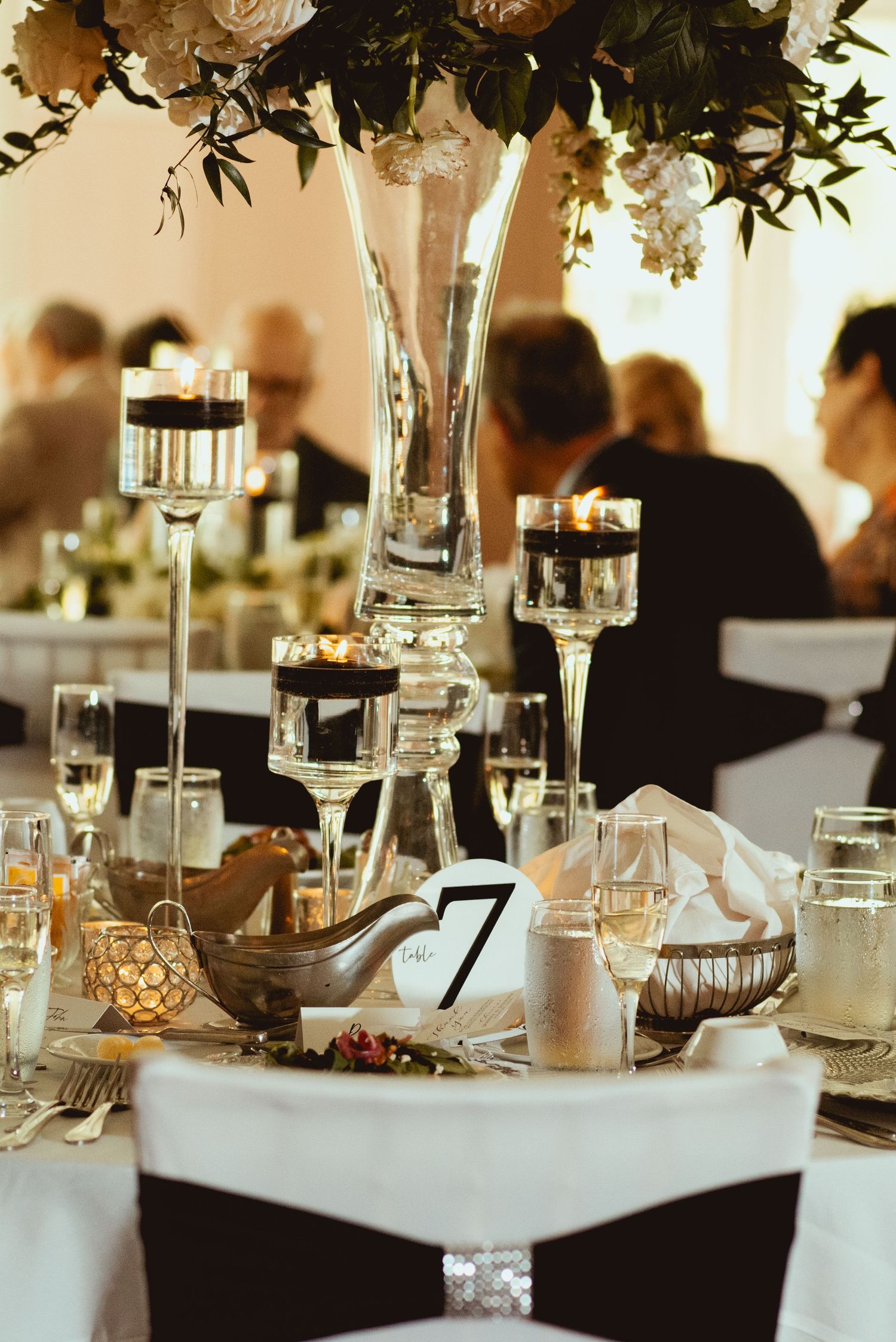 Elegant wedding table settings with tall floral centerpieces and crystal glassware.