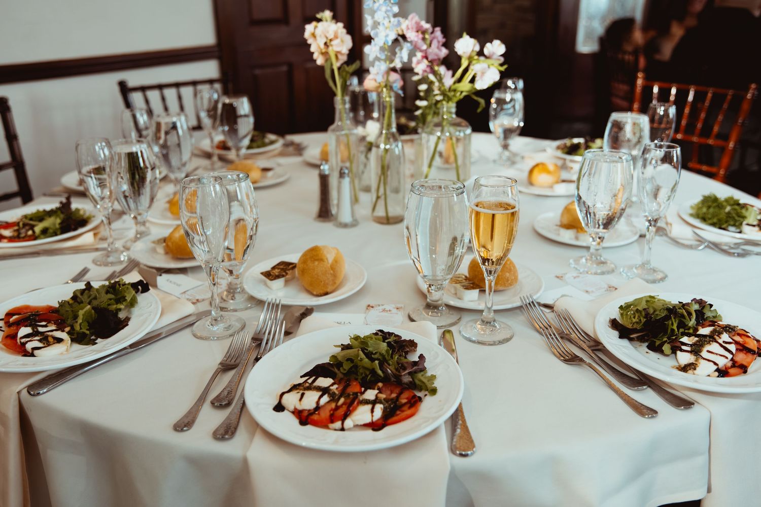 Elegant wedding reception table set with white linens, salad plates, and champagne glasses.