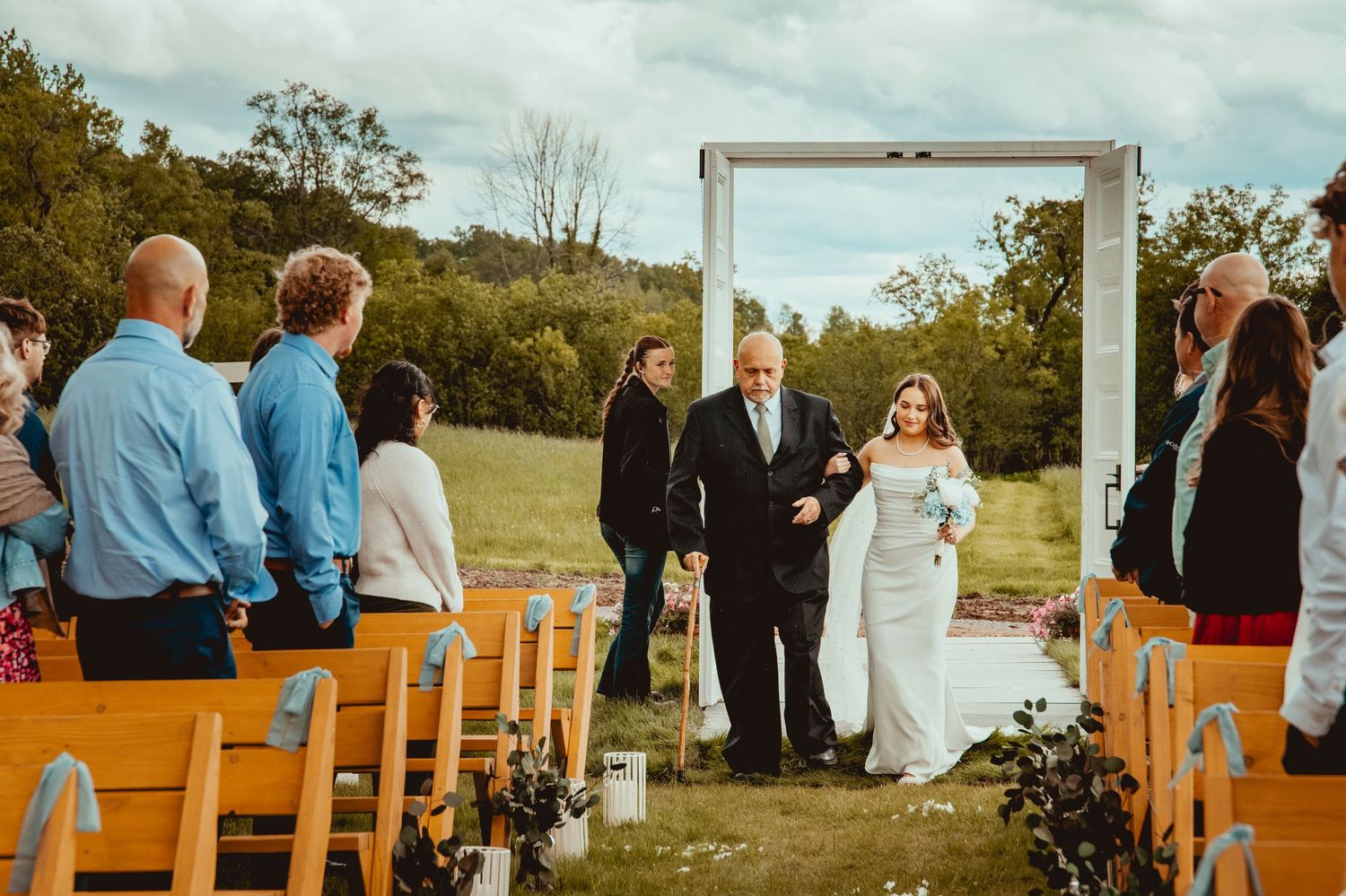 Wedding guests seated on wooden benches witnessing an outdoor ceremony with decorative white doors.
