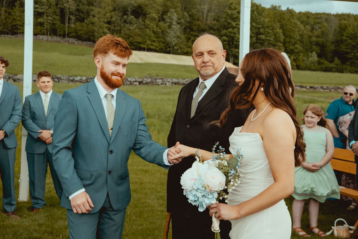 Wedding party poses for formal photos outdoors with mountains in background.