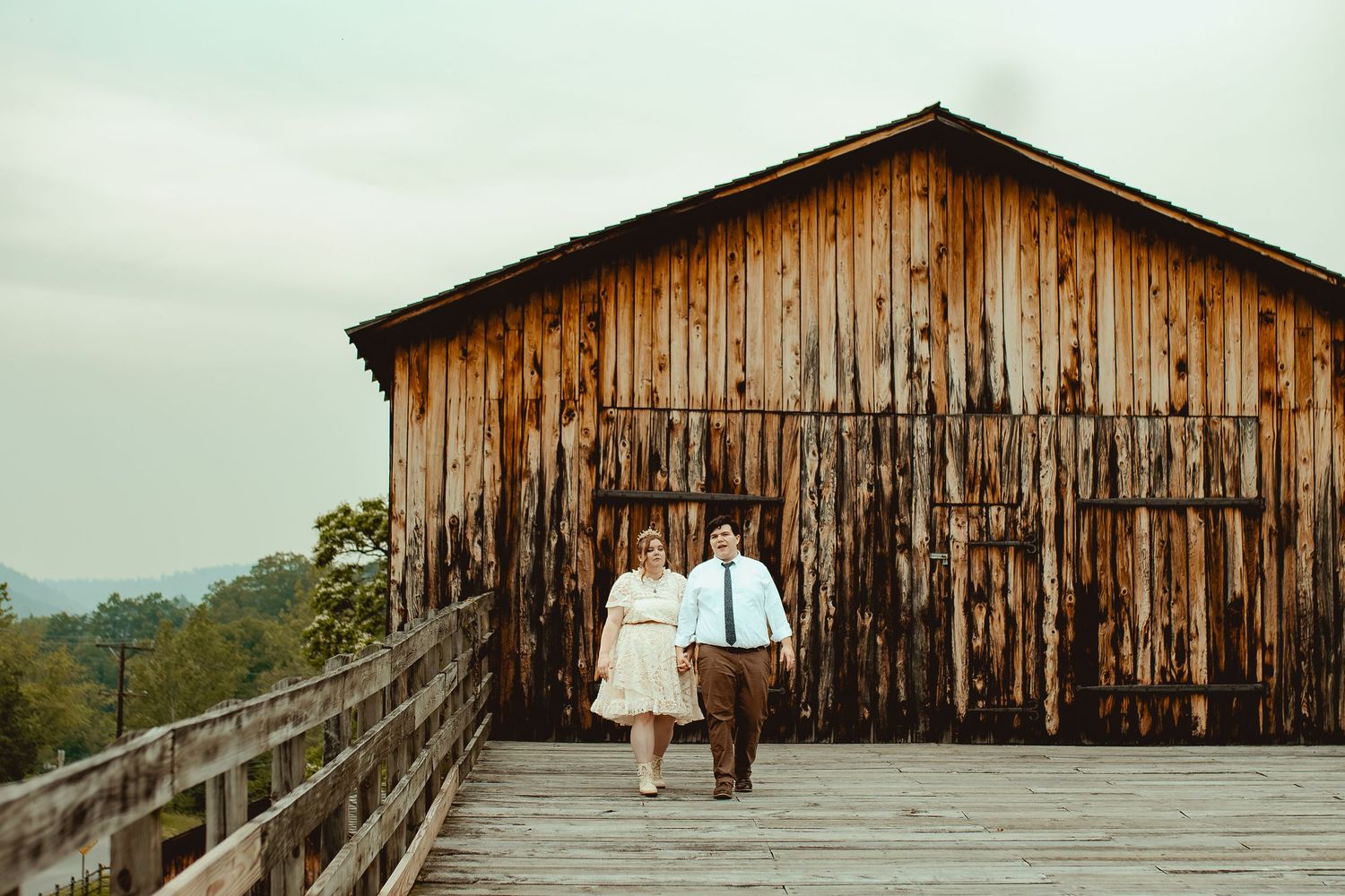 A rustic wooden barn with weathered siding stands against a scenic mountain backdrop in warm evening light.