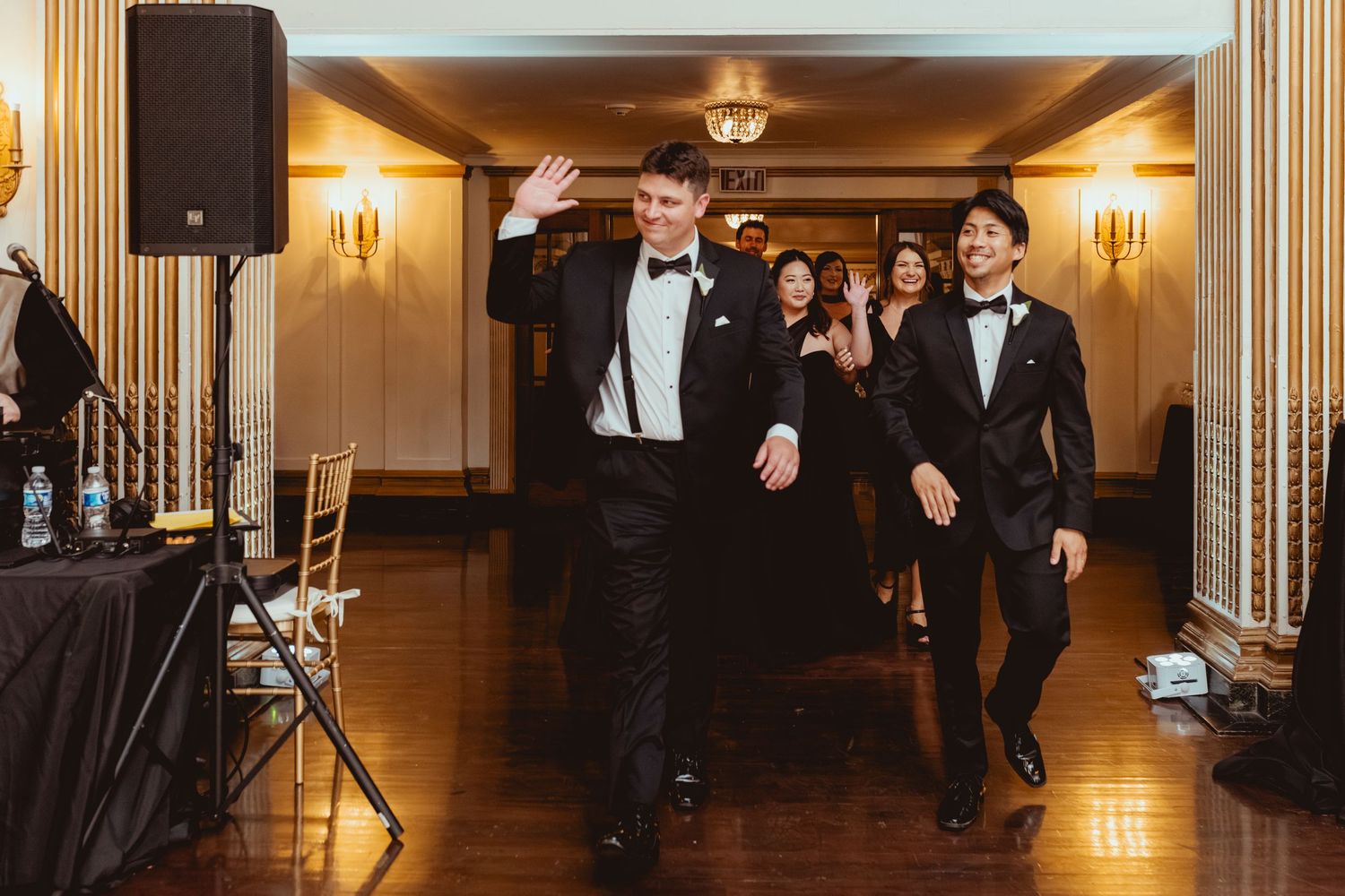 Wedding reception guests dancing and celebrating in an elegant ballroom with warm lighting.