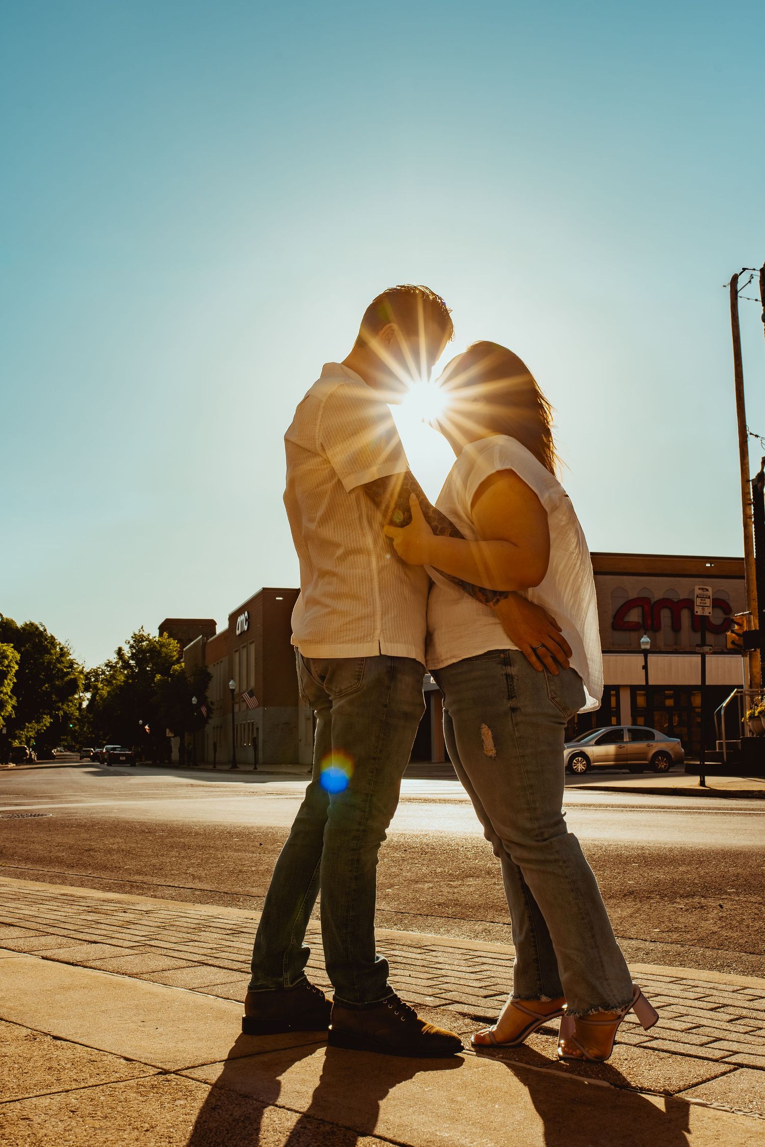 A couple embracing on a sunny street corner with a beautiful sunburst shining between them.