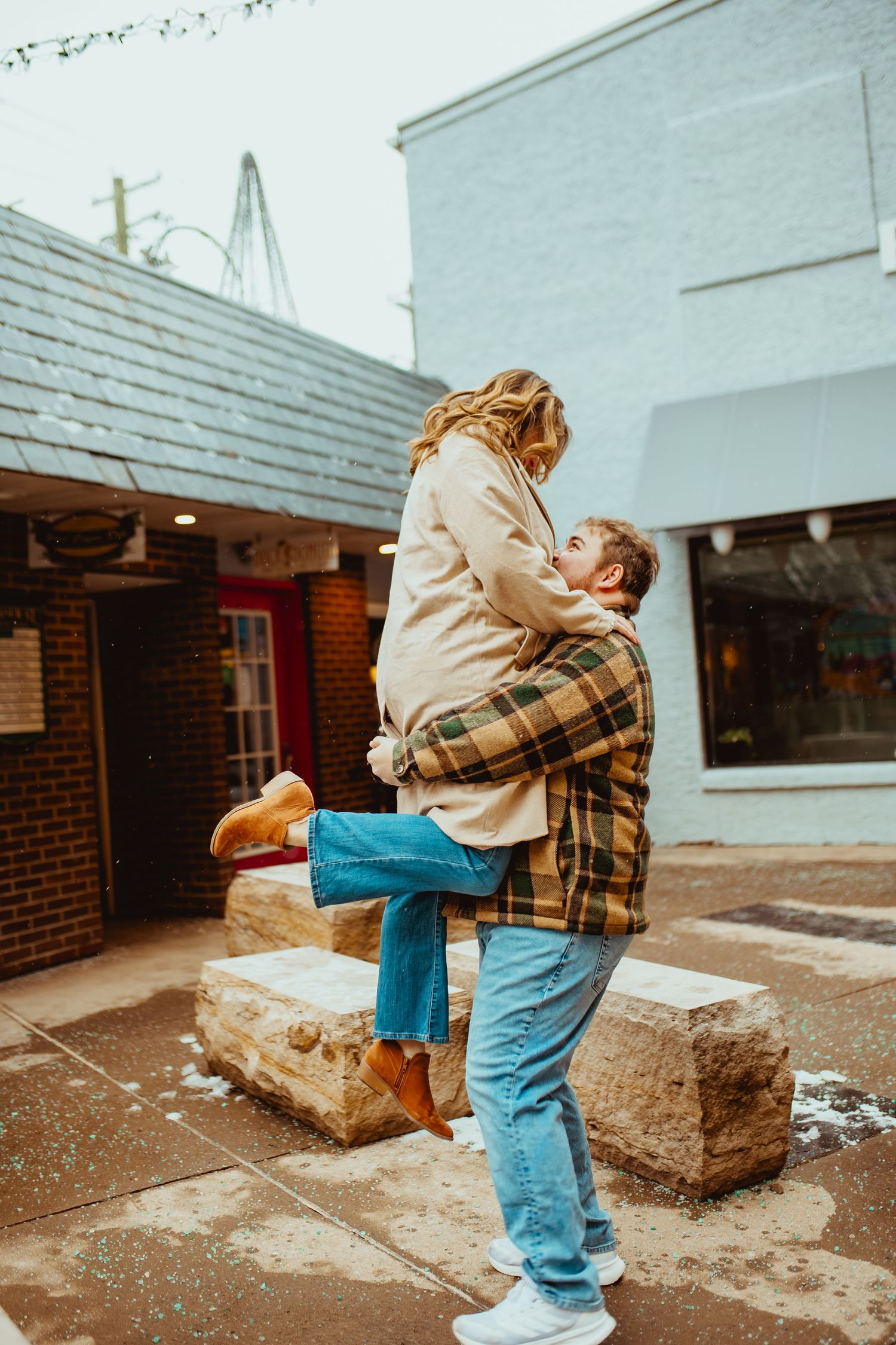 A couple embraces while sitting on concrete blocks outside a brick building on a winter day.
