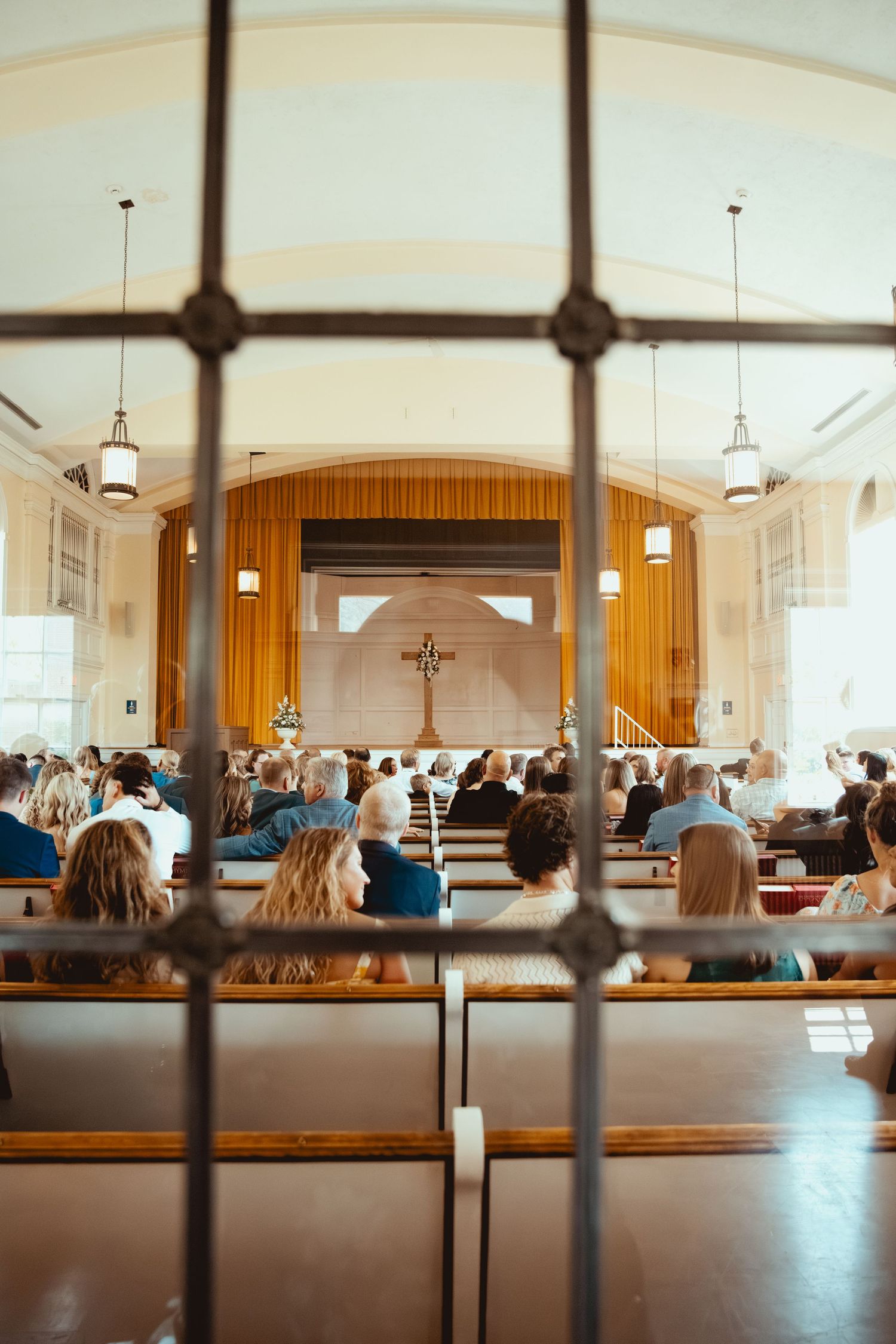 Interior view of a church sanctuary with wooden pews and cross at the altar during a wedding ceremony.