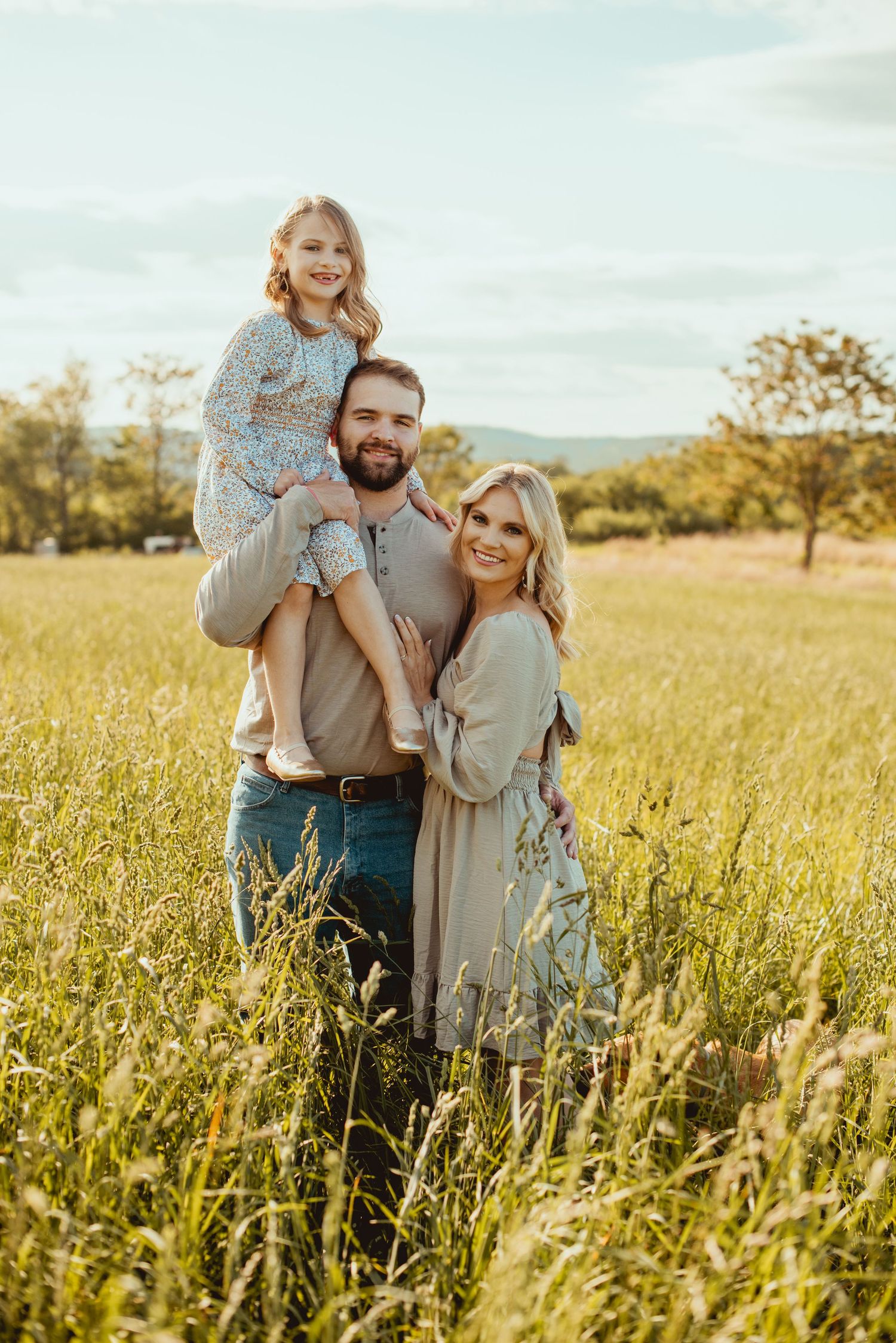 A family shares a tender moment together in a sunlit meadow of tall grass during golden hour.