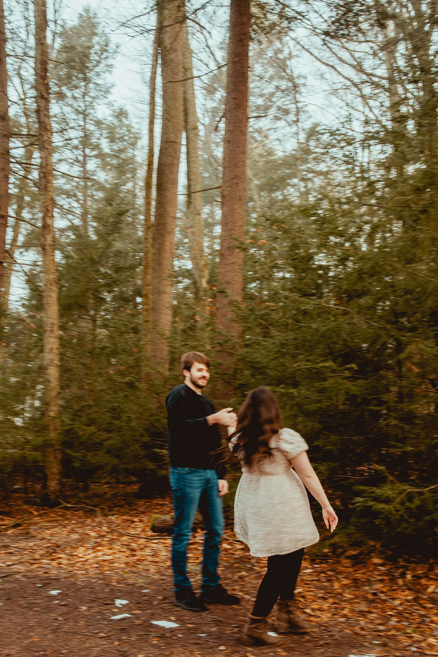 A romantic moment unfolds between two people in a foggy forest with fallen autumn leaves.