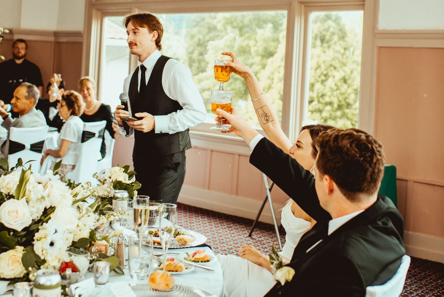 Reception guests raising glasses in celebration at tables decorated with white floral centerpieces.