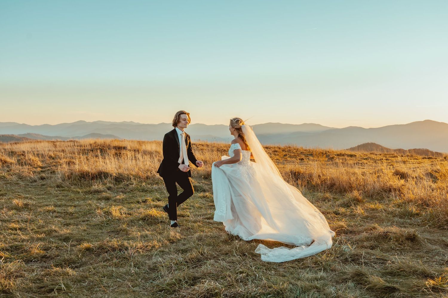 Wedding couple playfully walking through mountain field at sunset.