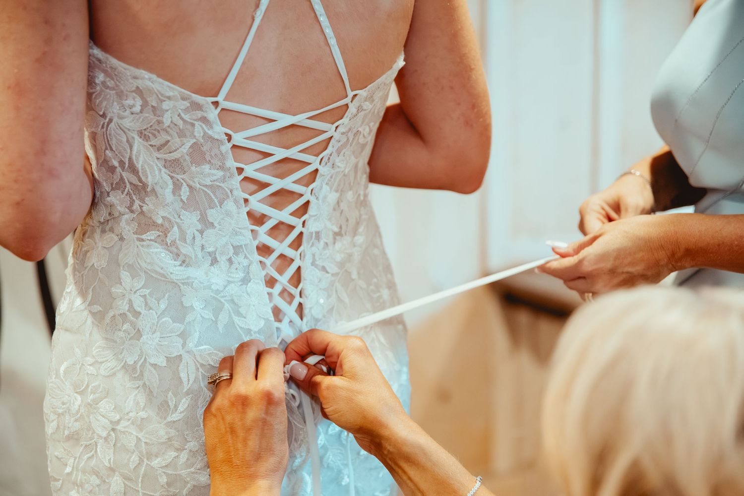 Wedding dress being laced up with intricate corset-style detail in white.