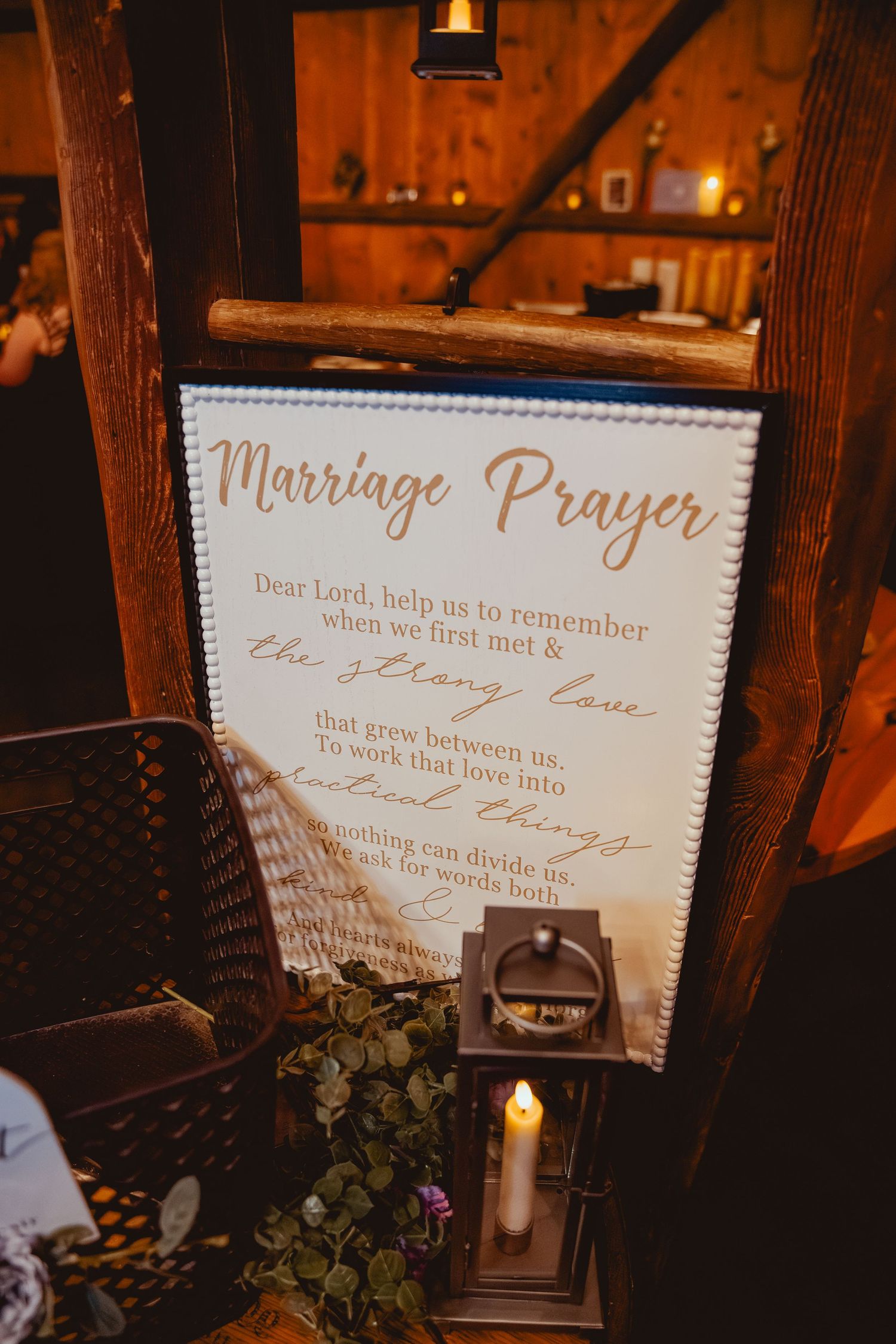 Wedding decor featuring a 'Marriage Prayer' sign and candle on wooden table in barn setting.
