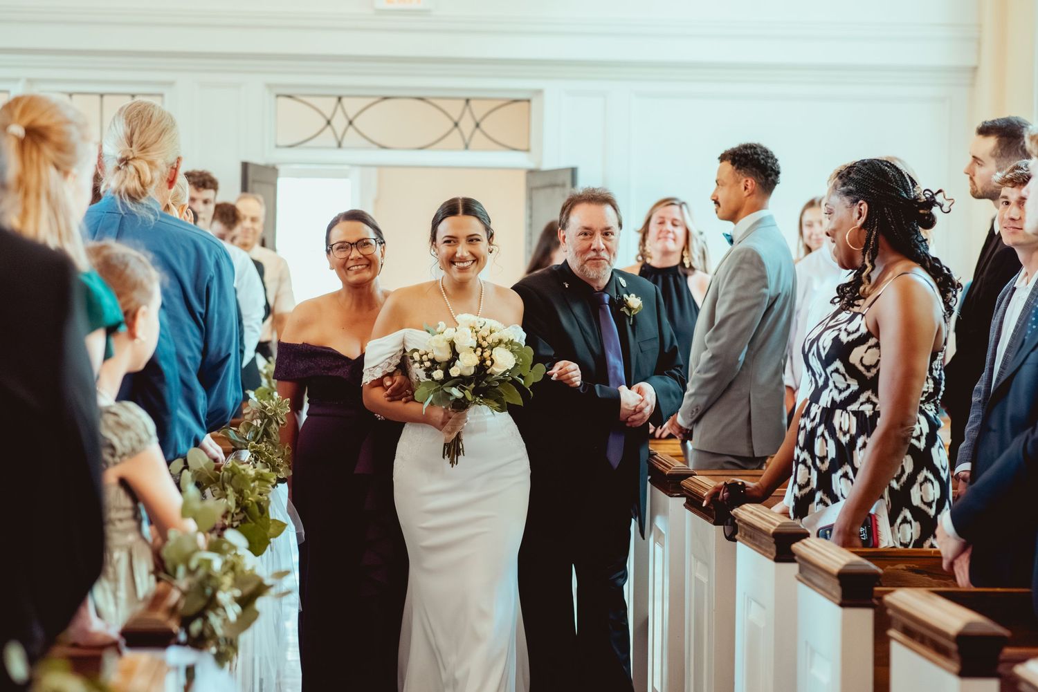 Wedding party lineup in a church with blue decor and natural lighting.