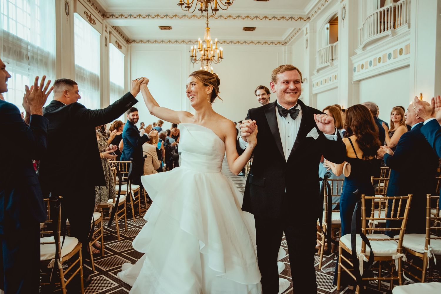 Wedding celebration in an elegant white ballroom with guests cheering and celebrating.