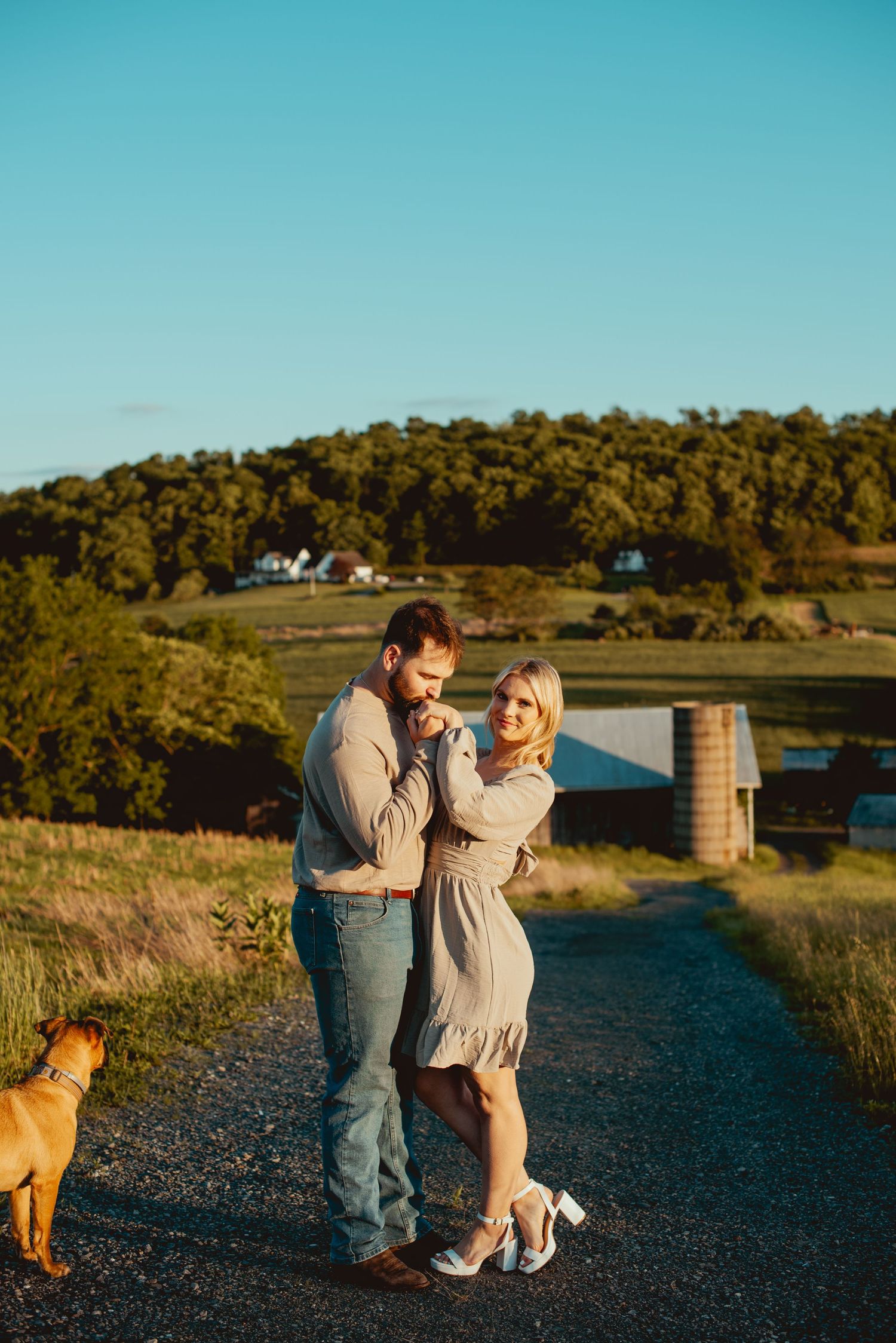 Couple dancing on a gravel path at sunset with their dog watching nearby.
