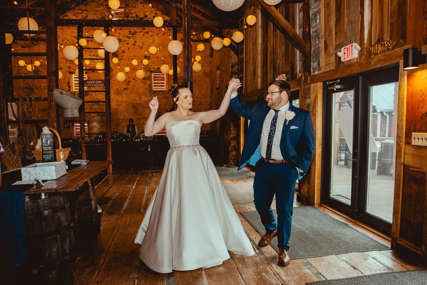 Bride and groom making grand entrance into rustic barn reception venue with string lights and lanterns.